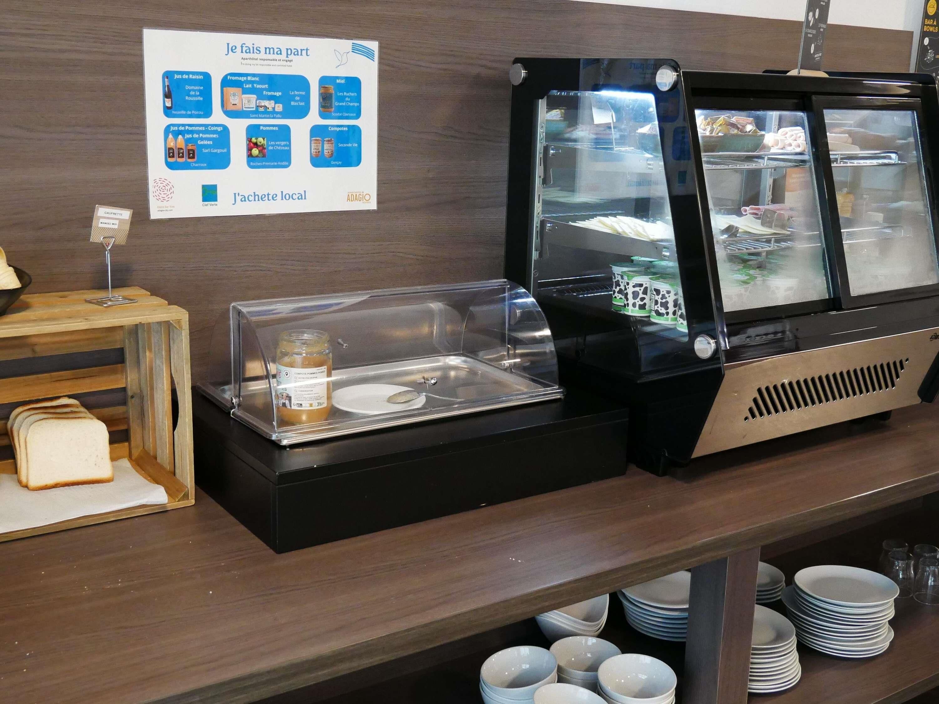 A buffet area with a sign listing food items, a glass display case with a jar, and a stack of plates.