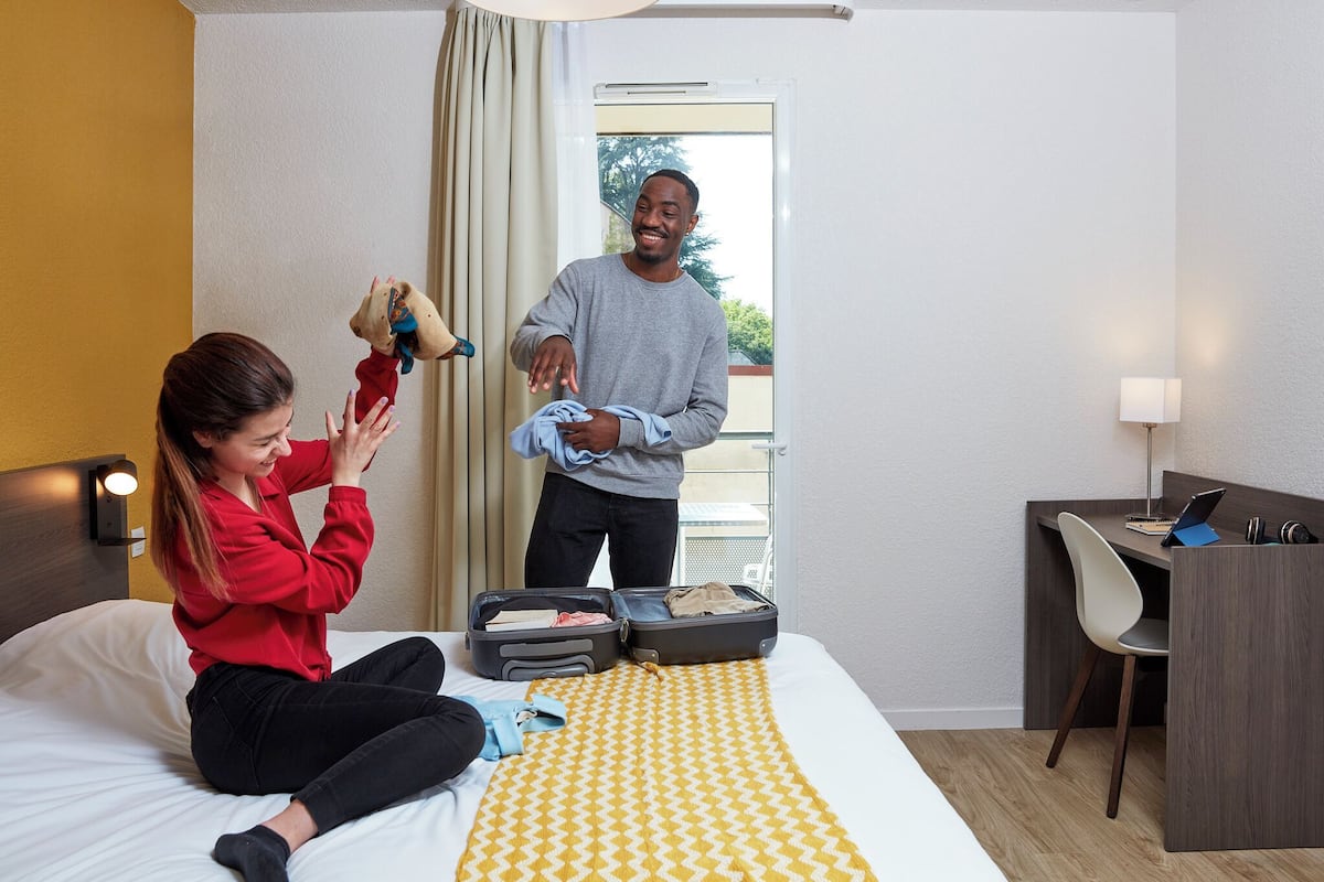 Ein Hotelzimmer mit Bett, Schreibtisch mit Stuhl und einem Koffer auf dem Bett.