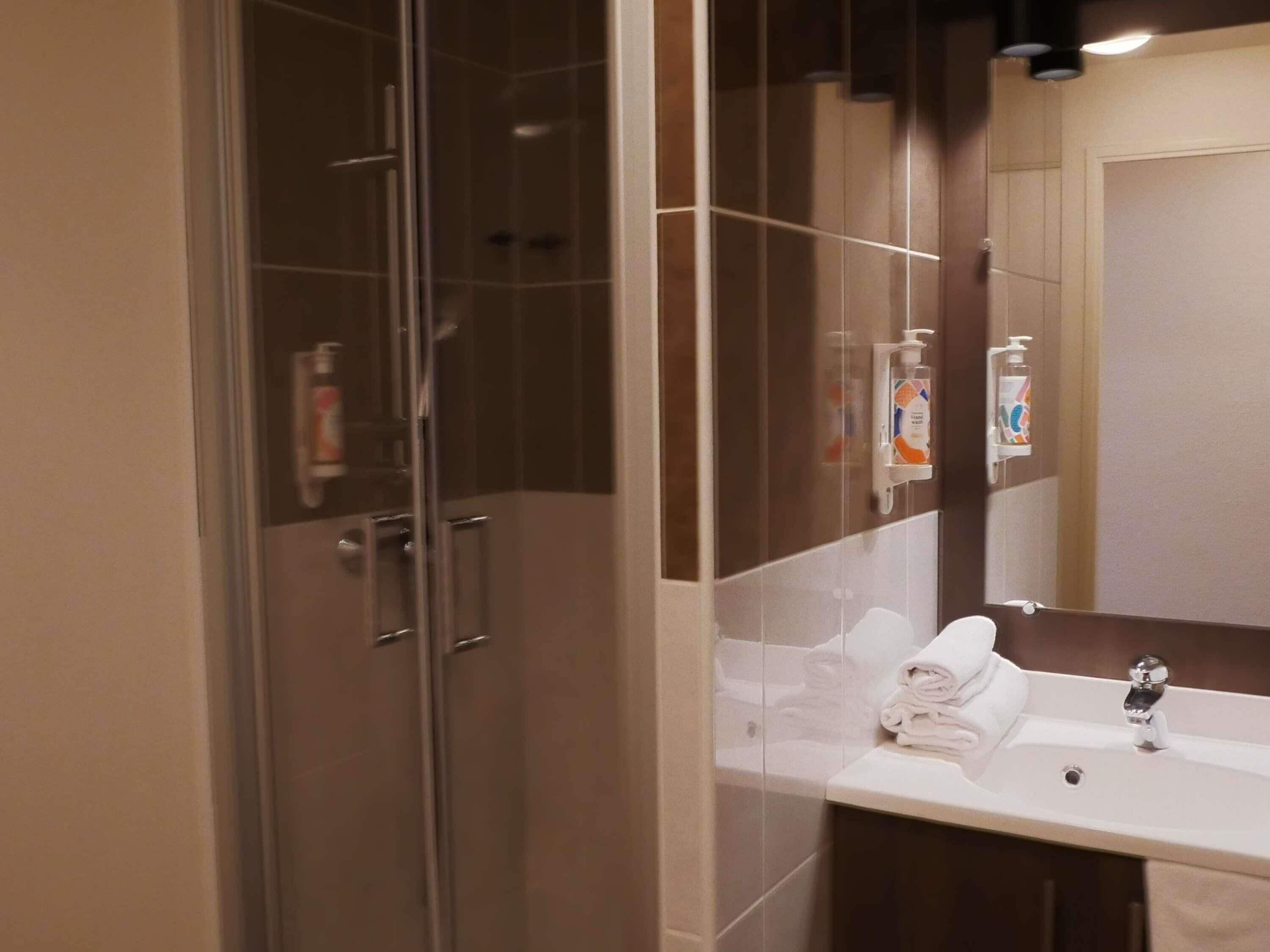 Een moderne badkamer met een douche met glazen wand, een wit wastafelmeubel met spiegel en toiletartikelen aan de muur.