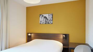 A hotel room with a bed, a desk, a chair, and a wall-mounted picture.