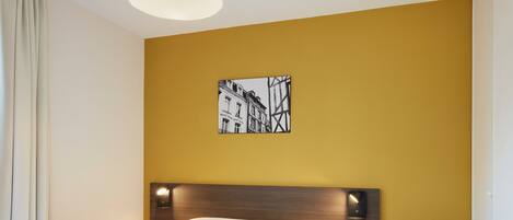 A hotel room with a bed, a desk, a chair, and a wall-mounted picture.