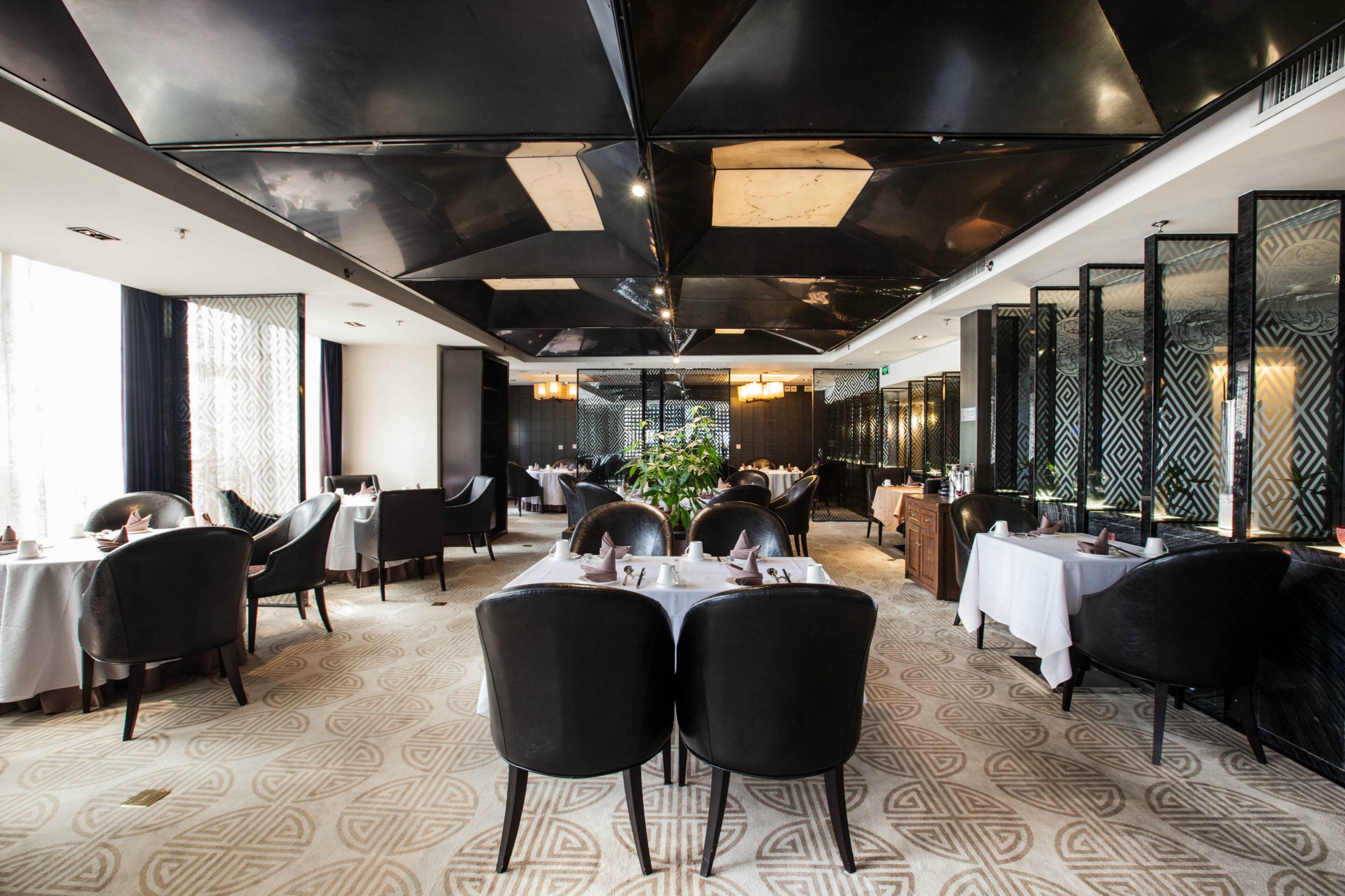 A modern dining area with tables set for service, black chairs, and patterned carpet.