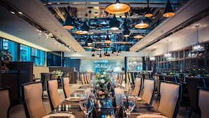 A restaurant with a long table set for dining, multiple hanging pendant lights, and a view of the kitchen in the background. - Holiday Inn Beijing Focus Square by IHG (Beijing)