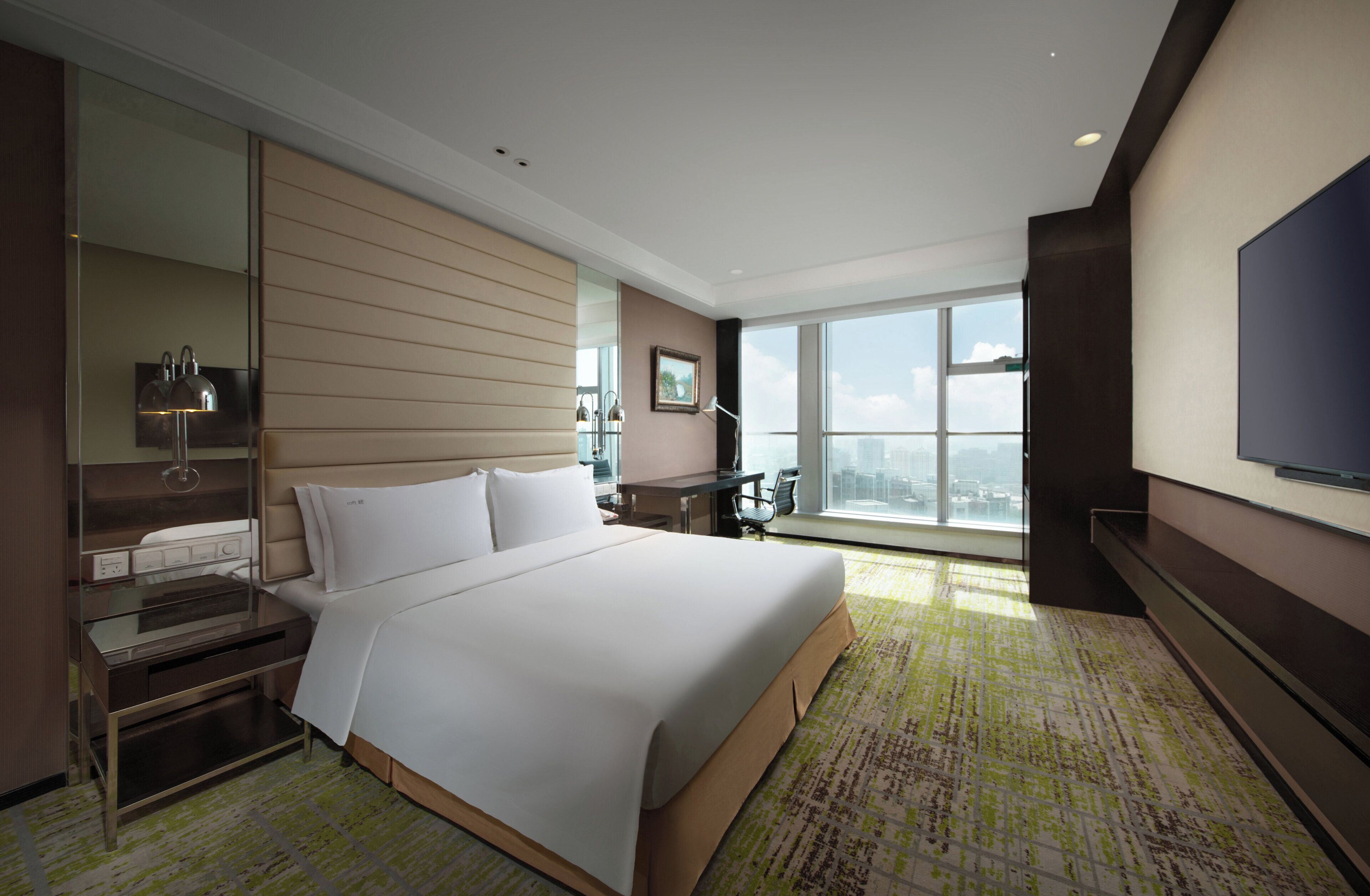 Habitación de hotel con una cama grande, un escritorio, una silla, un televisor y una ventana con vista a la ciudad.