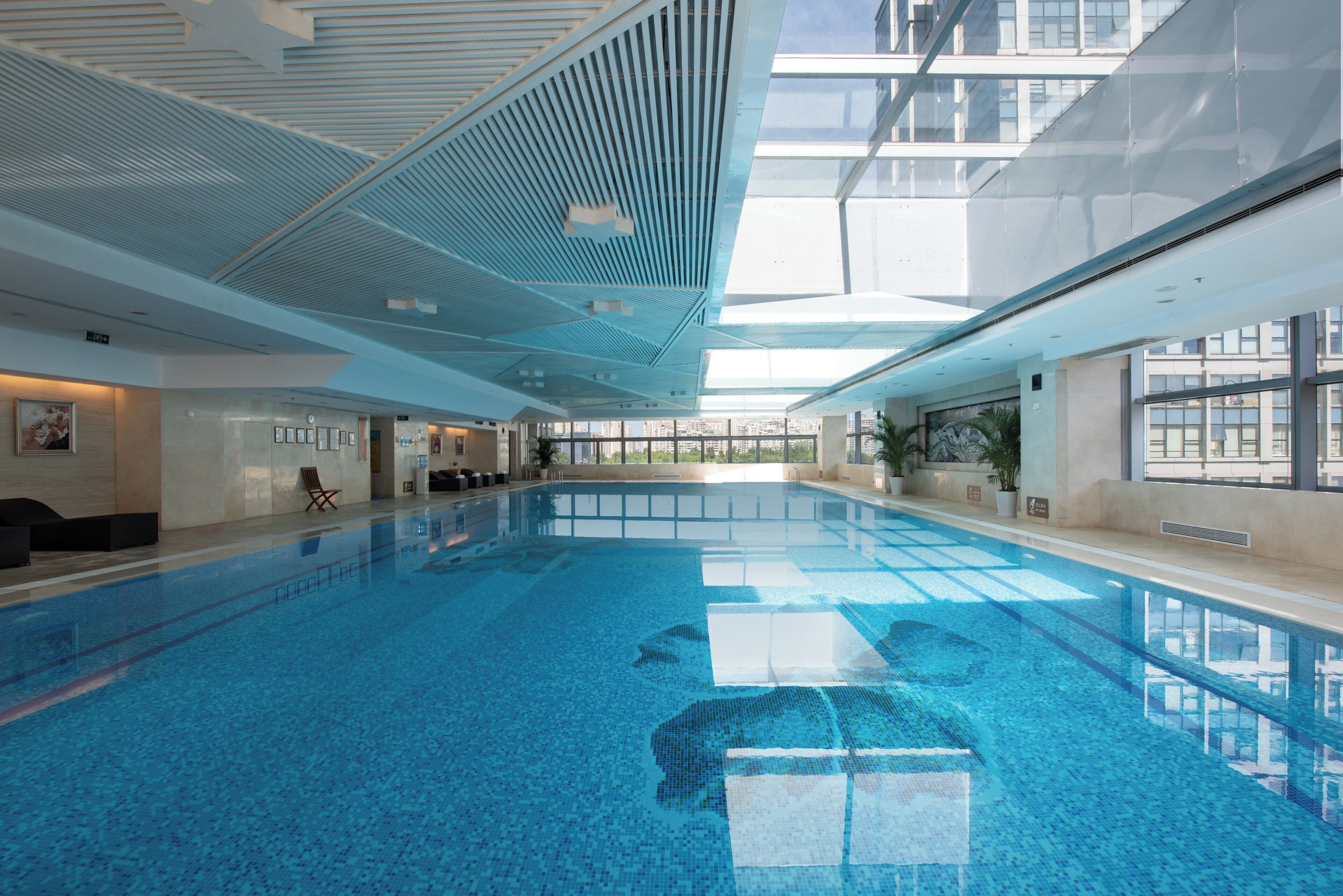 A large indoor swimming pool with clear blue water, surrounded by walls with framed pictures and a modern ceiling design.