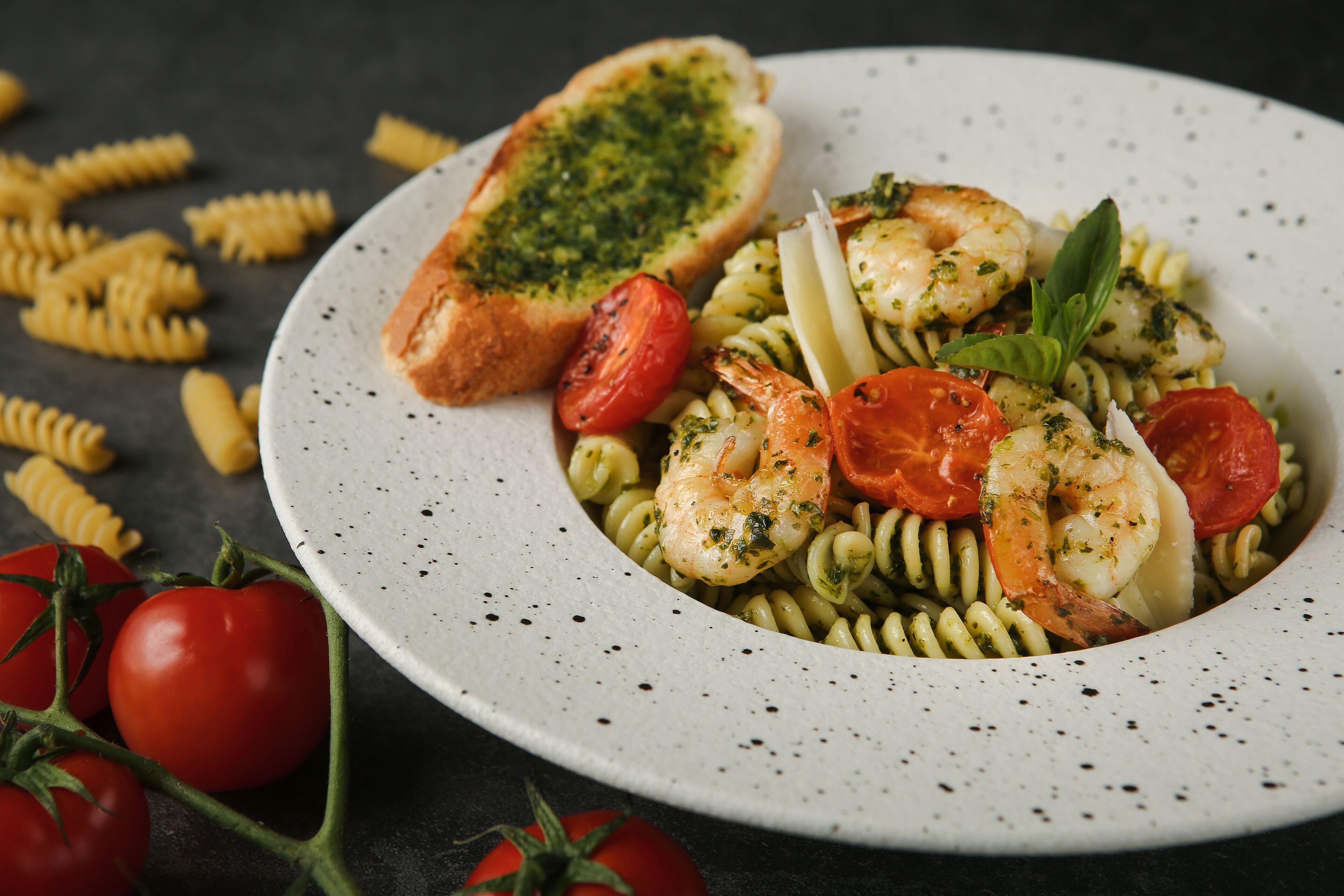 Een bord pasta met garnalen, tomaten en basilicum.