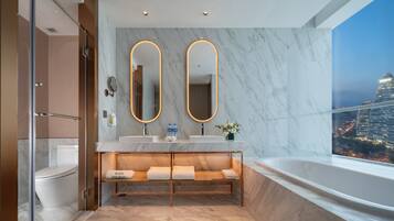 A modern bathroom with a large mirror, a vanity with a sink, a bench, and a bathtub.