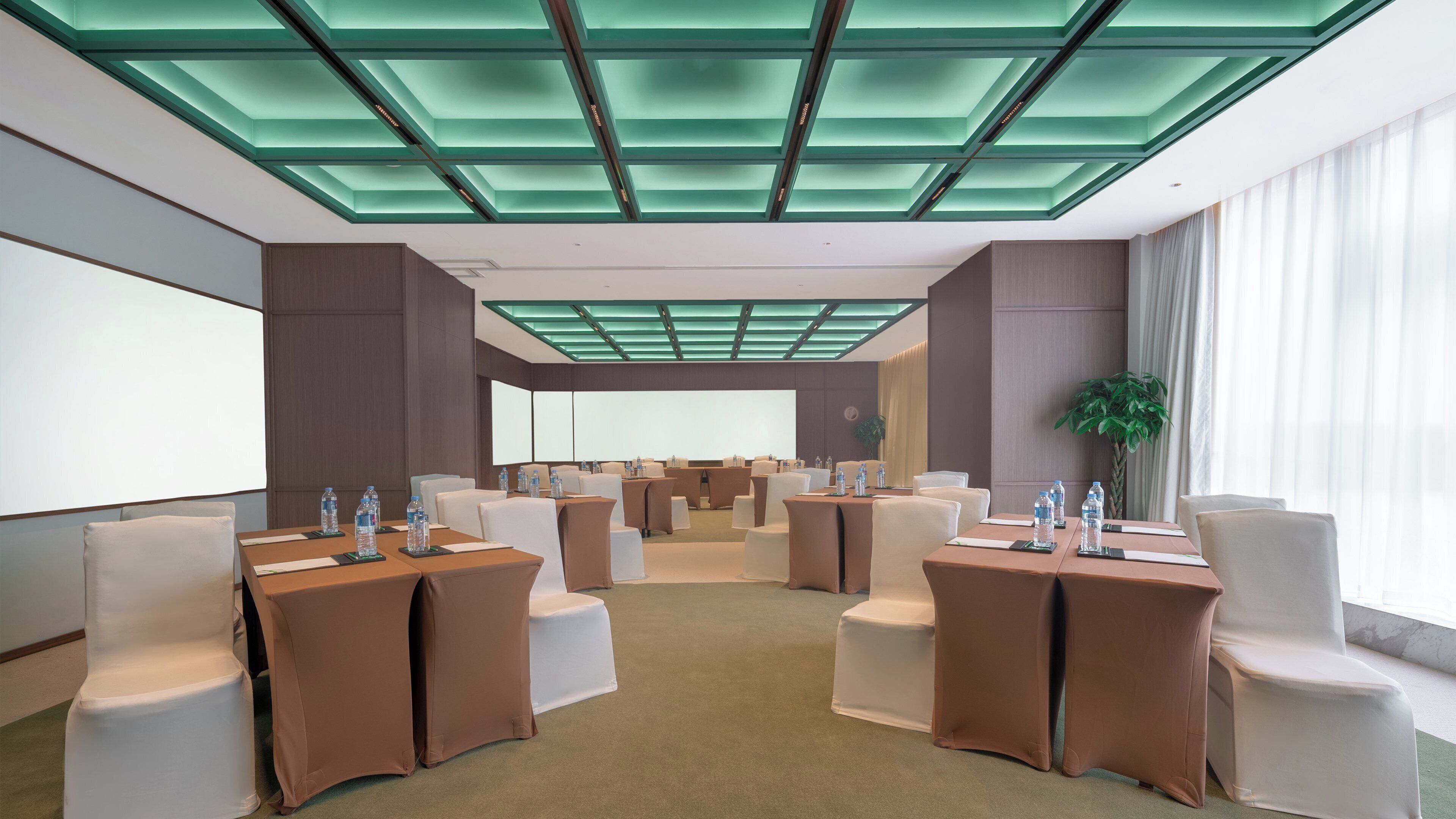 A conference room with a modern ceiling design, multiple tables with chairs, and a large screen.