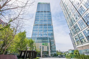 Un edificio hotelero alto con fachada de vidrio moderna, rodeado de árboles y otros edificios.
