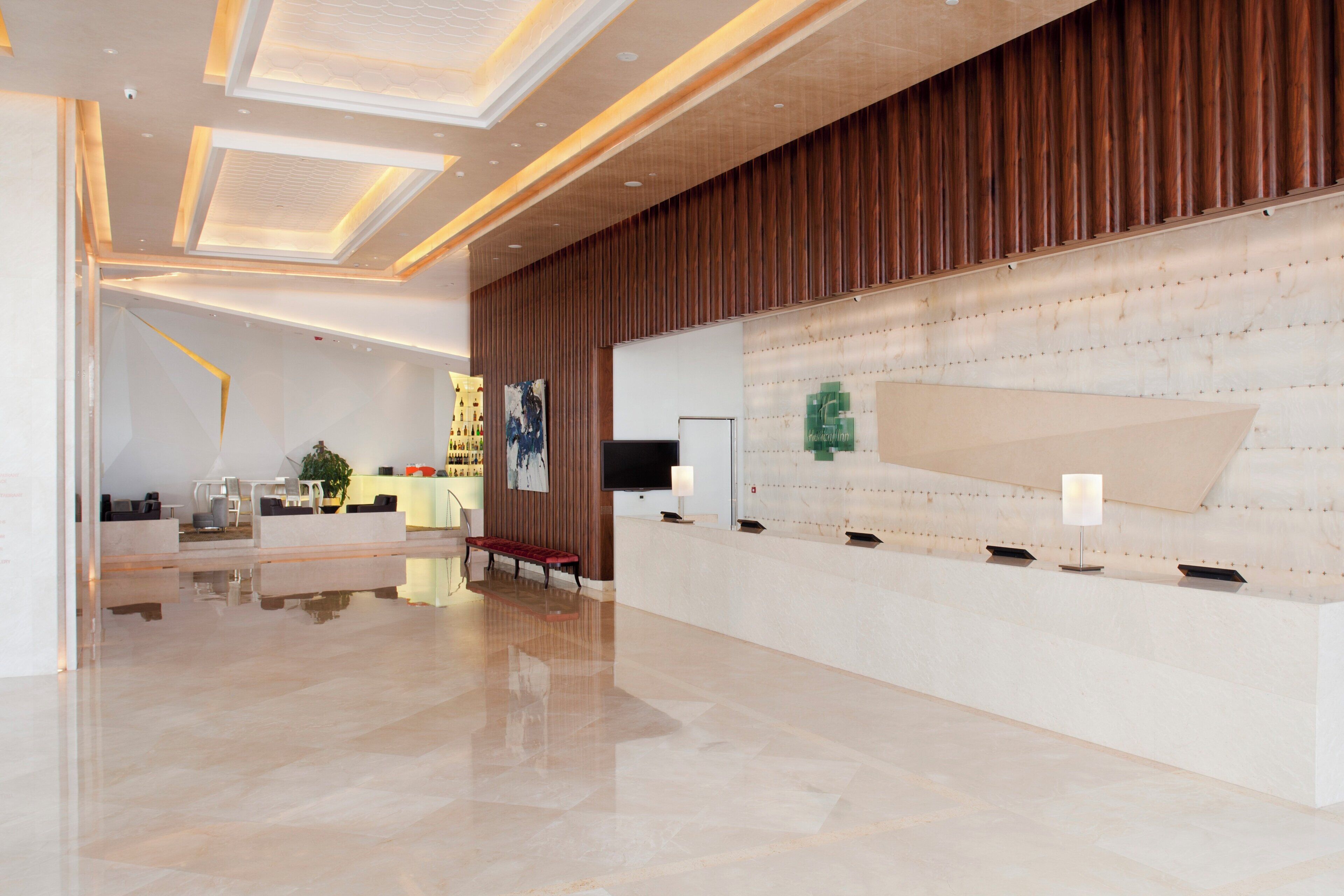 A modern hotel lobby with a reception desk, seating area, and a large wall with a decorative panel.