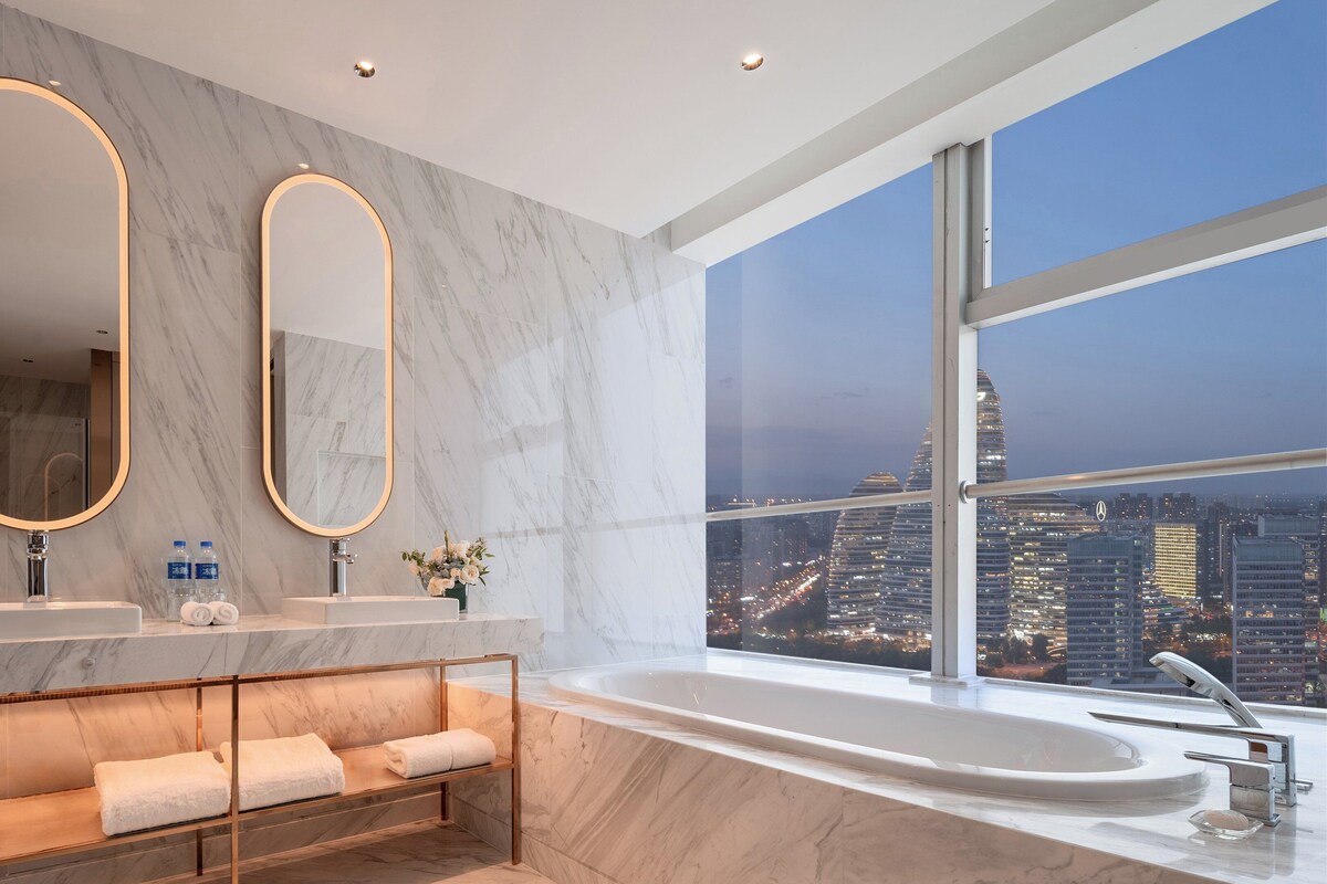 Un bagno moderno con due ampi specchi, una vasca da bagno e una panca con asciugamani.