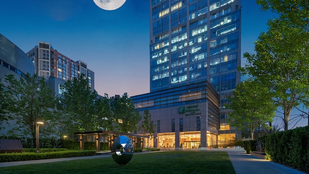 A modern hotel with a large glass facade, a well-maintained lawn, and a prominent moon in the sky. - Holiday Inn Beijing Focus Square by IHG (Beijing)
