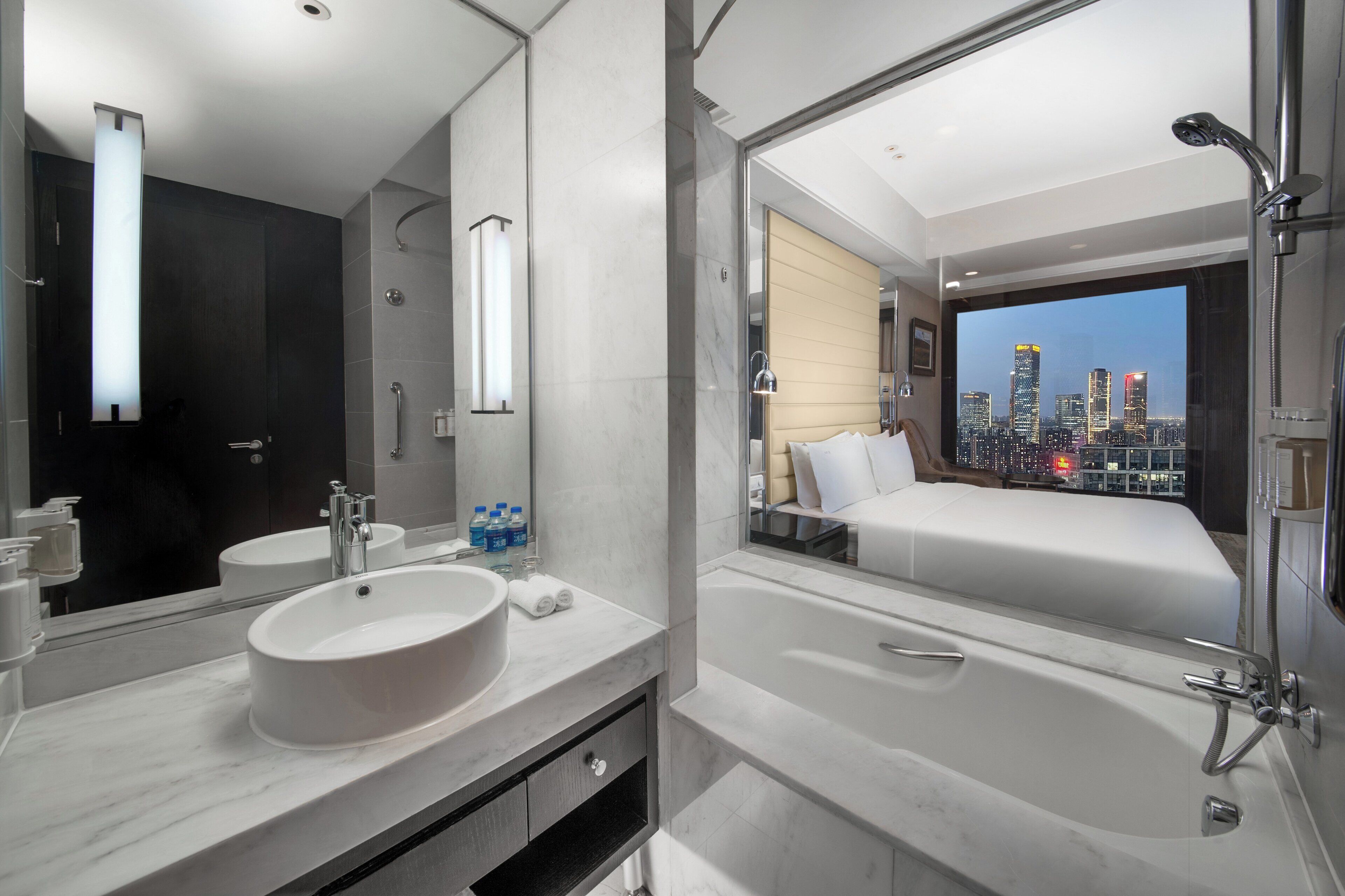 A modern bathroom with a large mirror, a sink, and a bathtub. There is a cityscape view through the window.