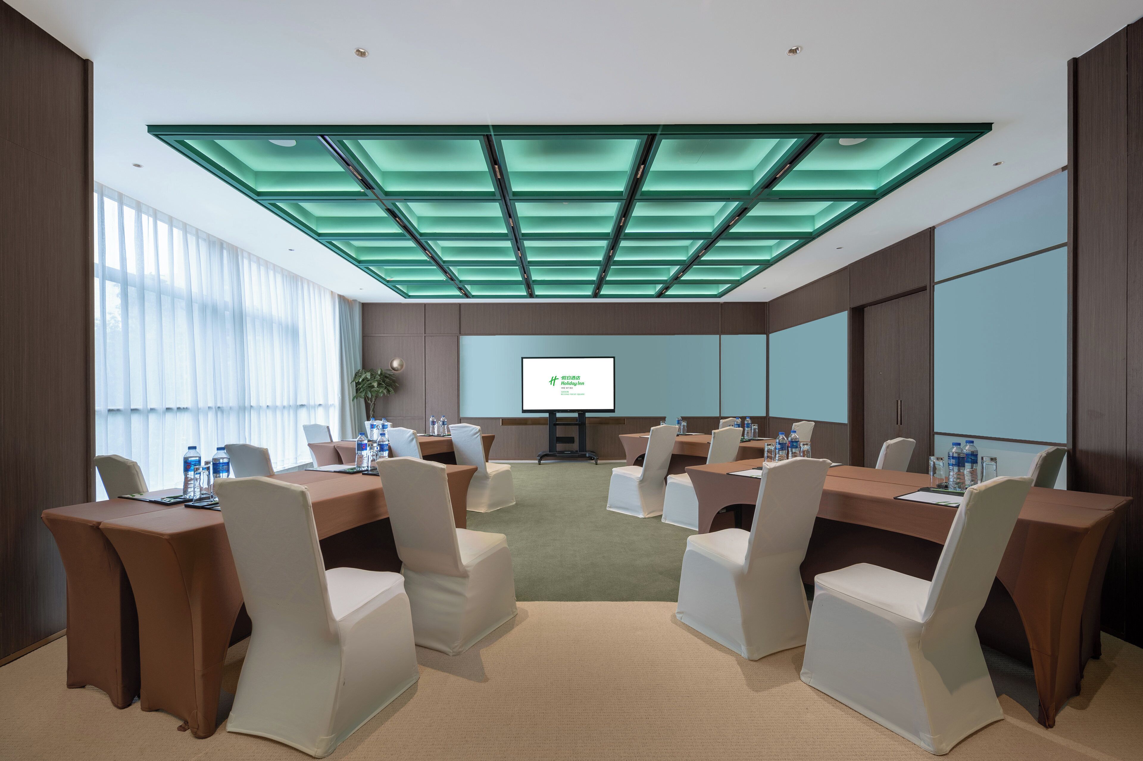 A conference room with a modern design, featuring a large table surrounded by chairs, a projector screen, and a glass ceiling.