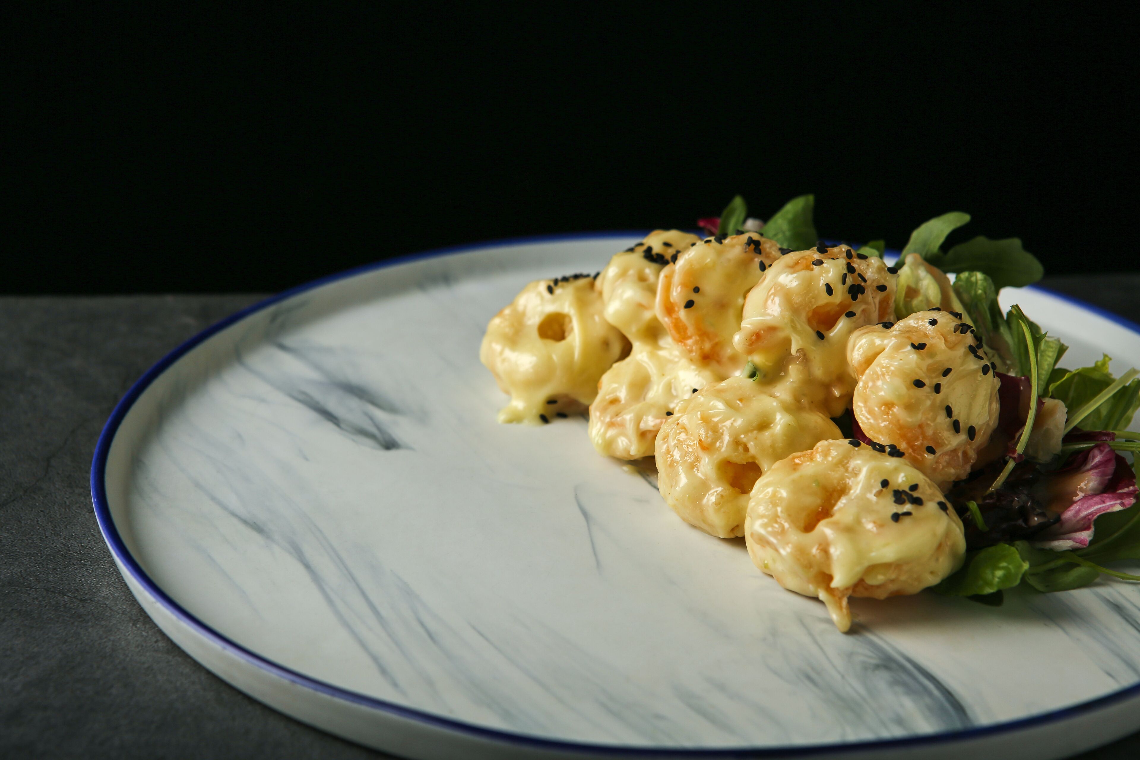 Een bord met macaronischoteltje met kaasballetjes, versierd met zwarte sesamzaadjes, op een wit bord met blauwe rand.