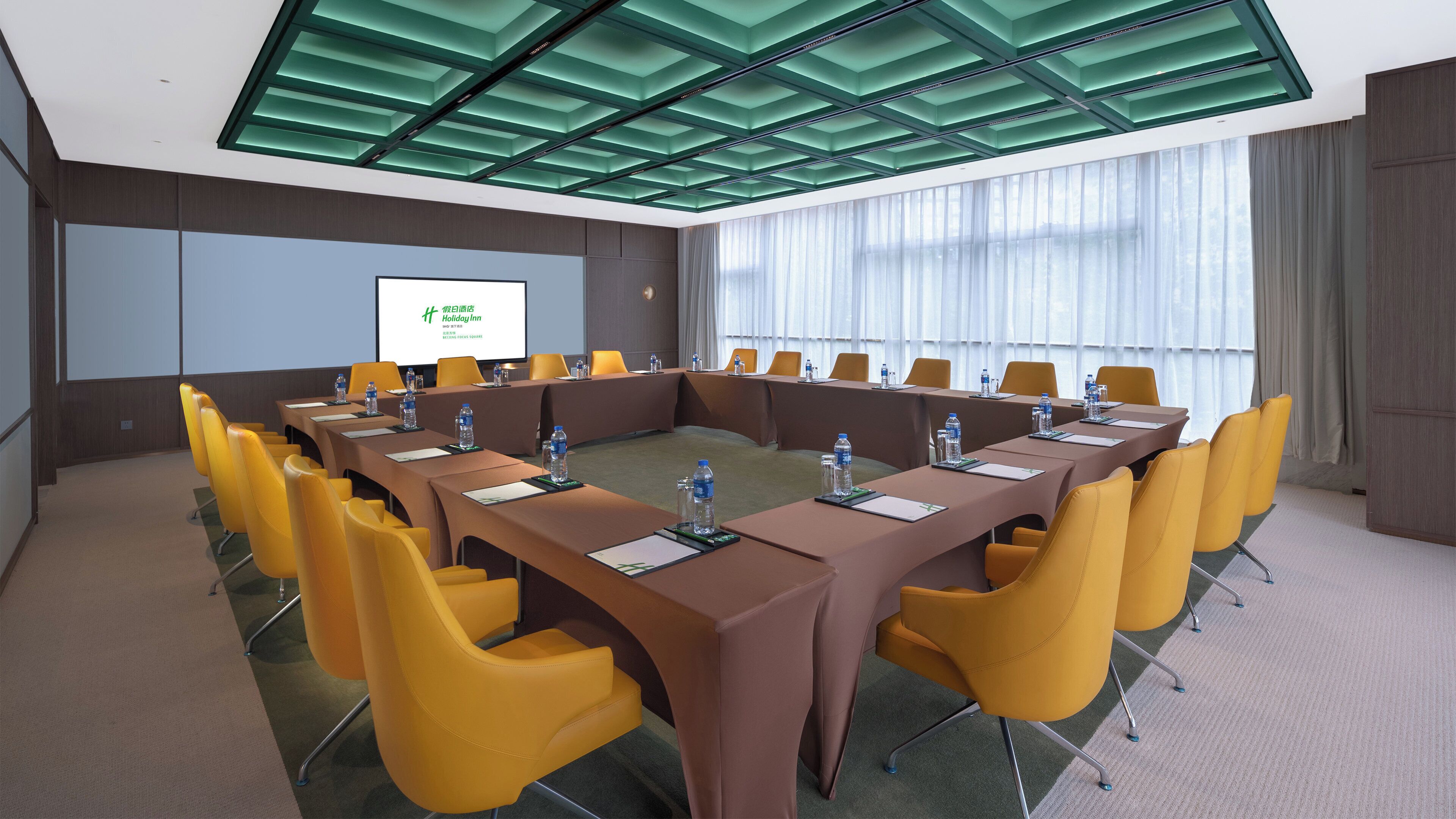 A conference room with a long table, yellow chairs, and a projector screen.