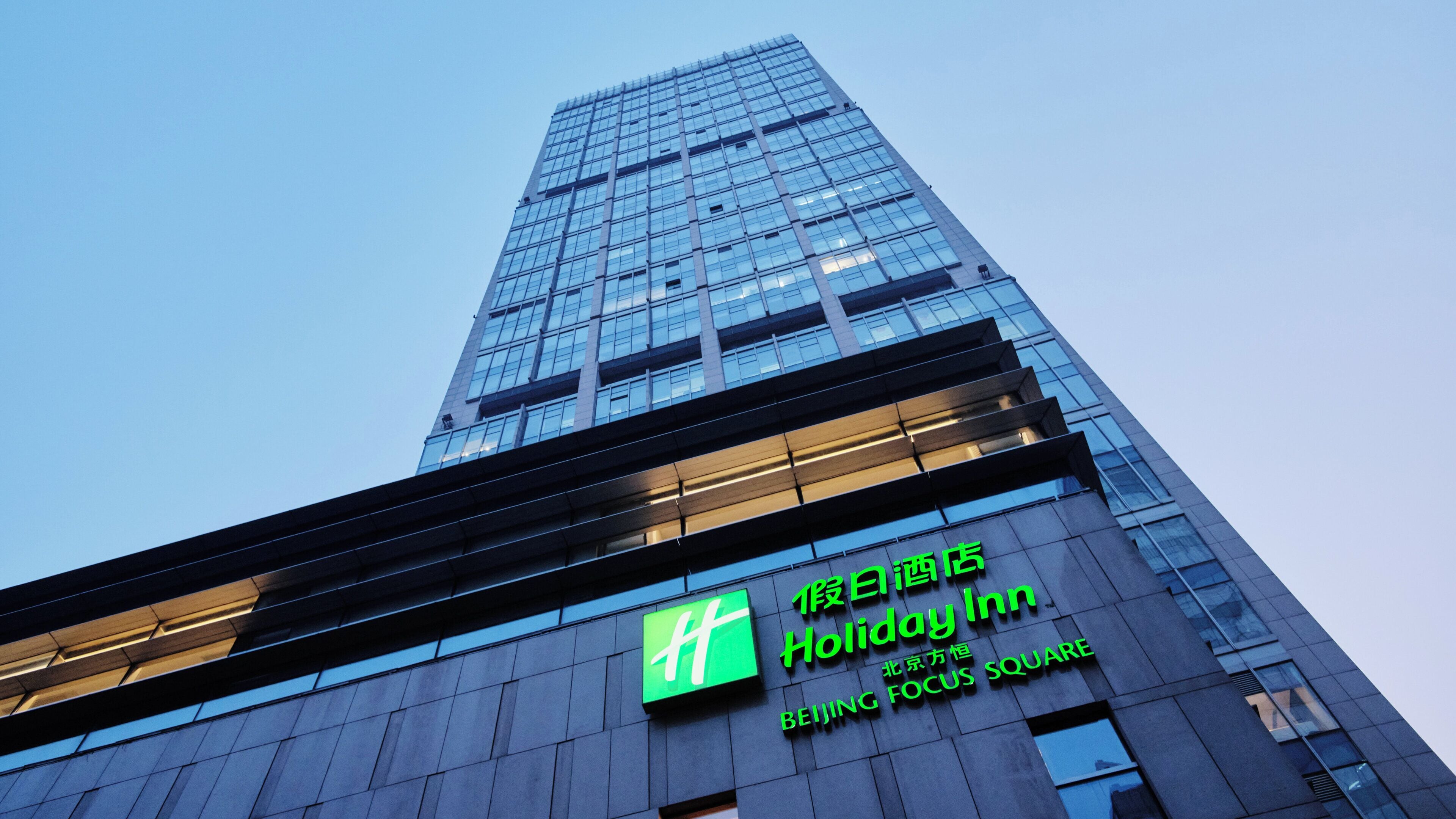 A tall building with a green sign for Holiday Inn Beijing.