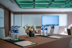 A conference room with a table set for a meeting, water bottles, a flower vase, and a large screen in the background.