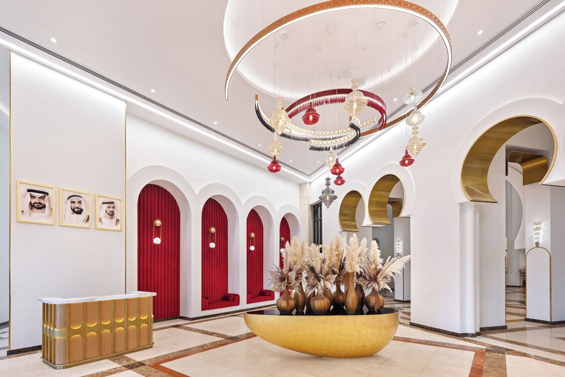 Un vestíbulo con mostrador de recepción, cortinas rojas y un recipiente decorativo grande con plantas.