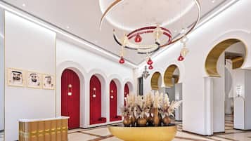 Un vestíbulo con mostrador de recepción, cortinas rojas y un recipiente decorativo grande con plantas.