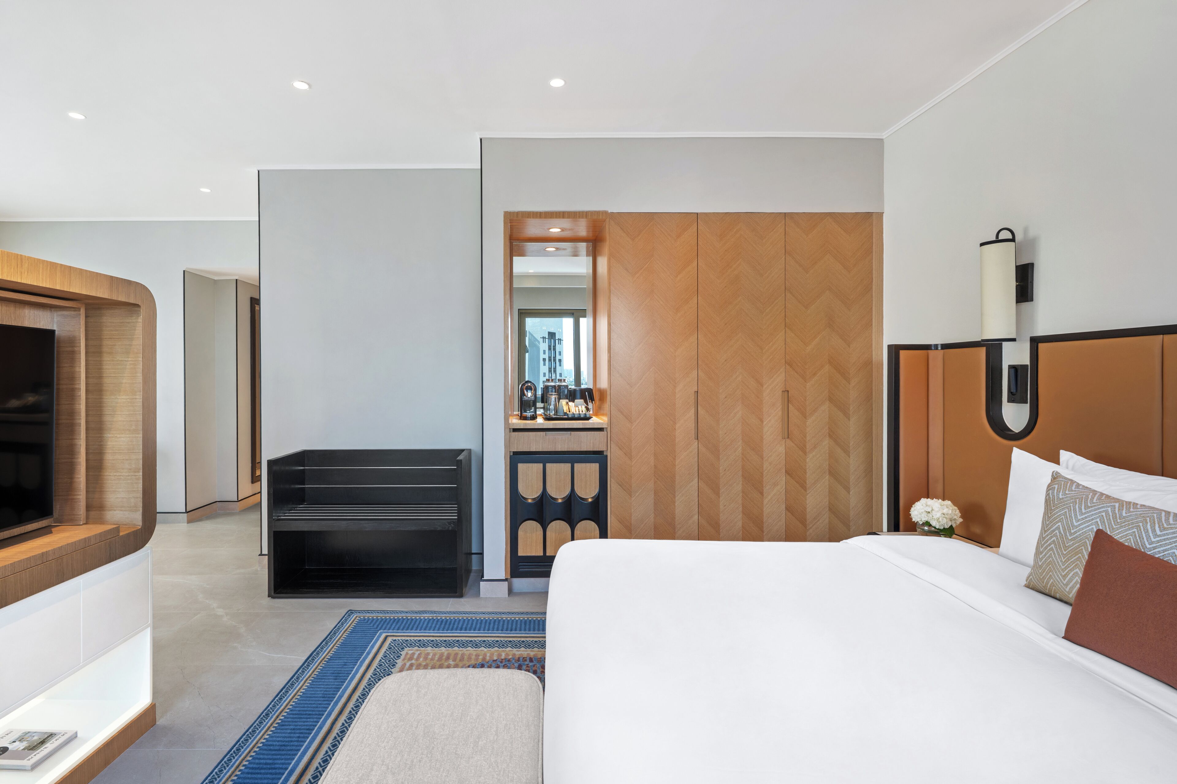 A hotel room with a bed, a TV, a desk with a chair, and a bathroom visible through a door.