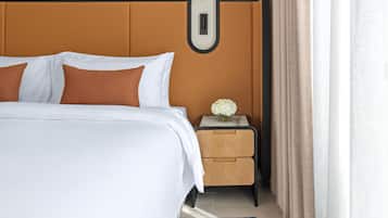 A neatly made bed with white and brown pillows, a bedside table with a vase of flowers, and a wall-mounted light fixture.