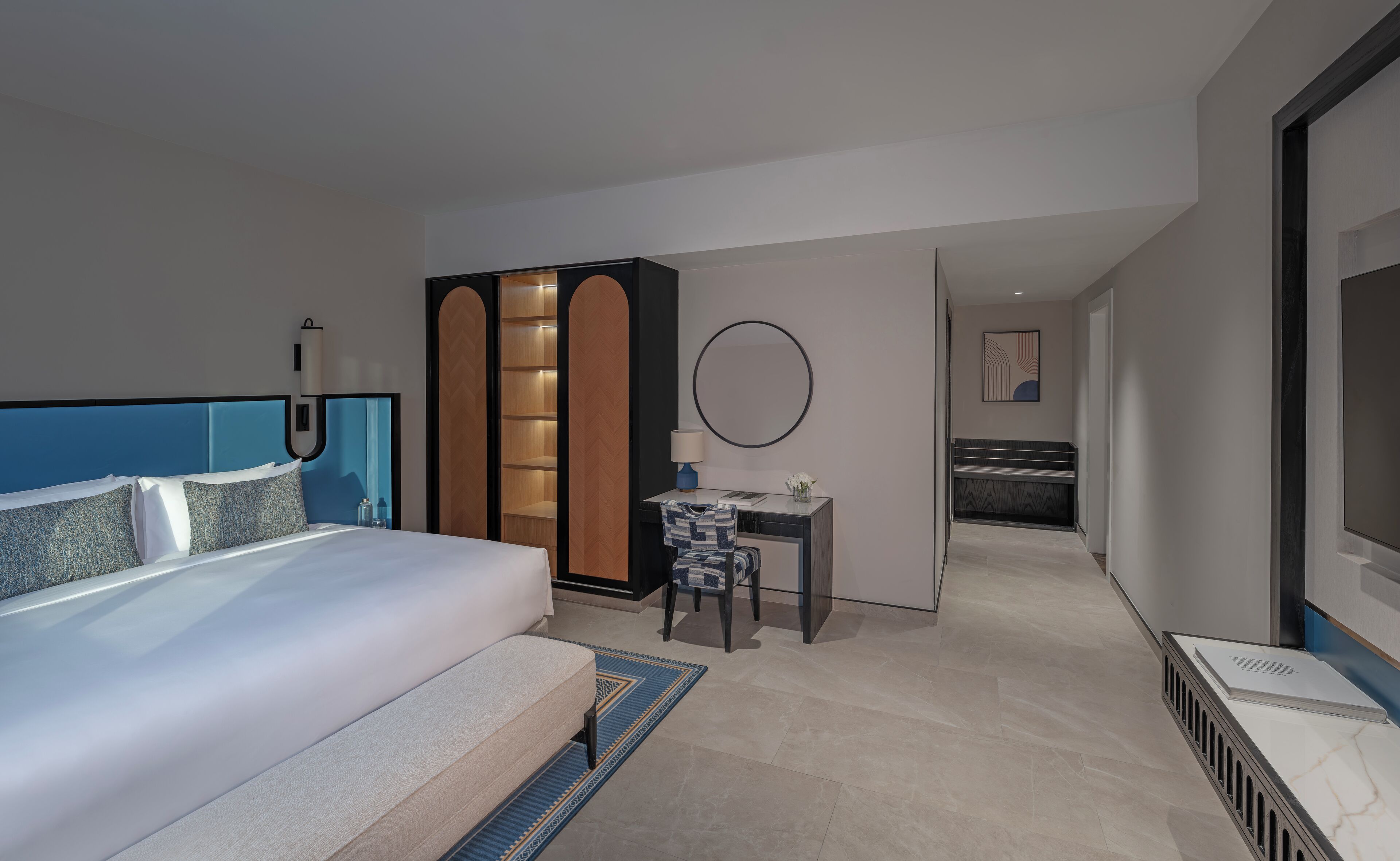 Une chambre d’hôtel moderne, dotée d’un grand lit, d’un bureau, d’une armoire et d’une salle de bain visible à travers une porte ouverte.