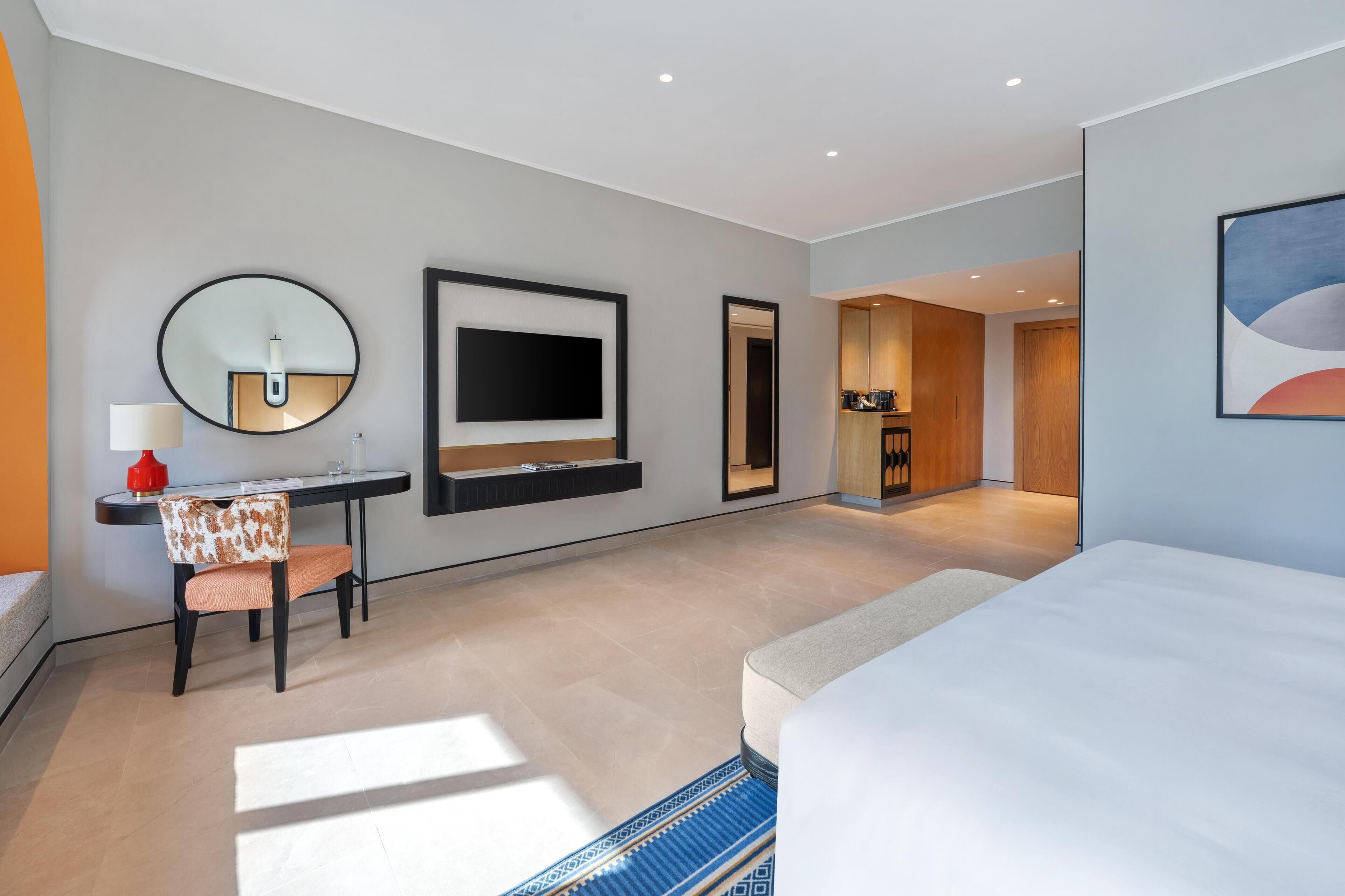 Een moderne hotelkamer met een groot bed, een bureau met stoel, een flatscreen-tv aan de muur en een kitchenette.
