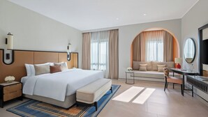A modern hotel room with a large bed, a sofa, a desk, and a TV.
