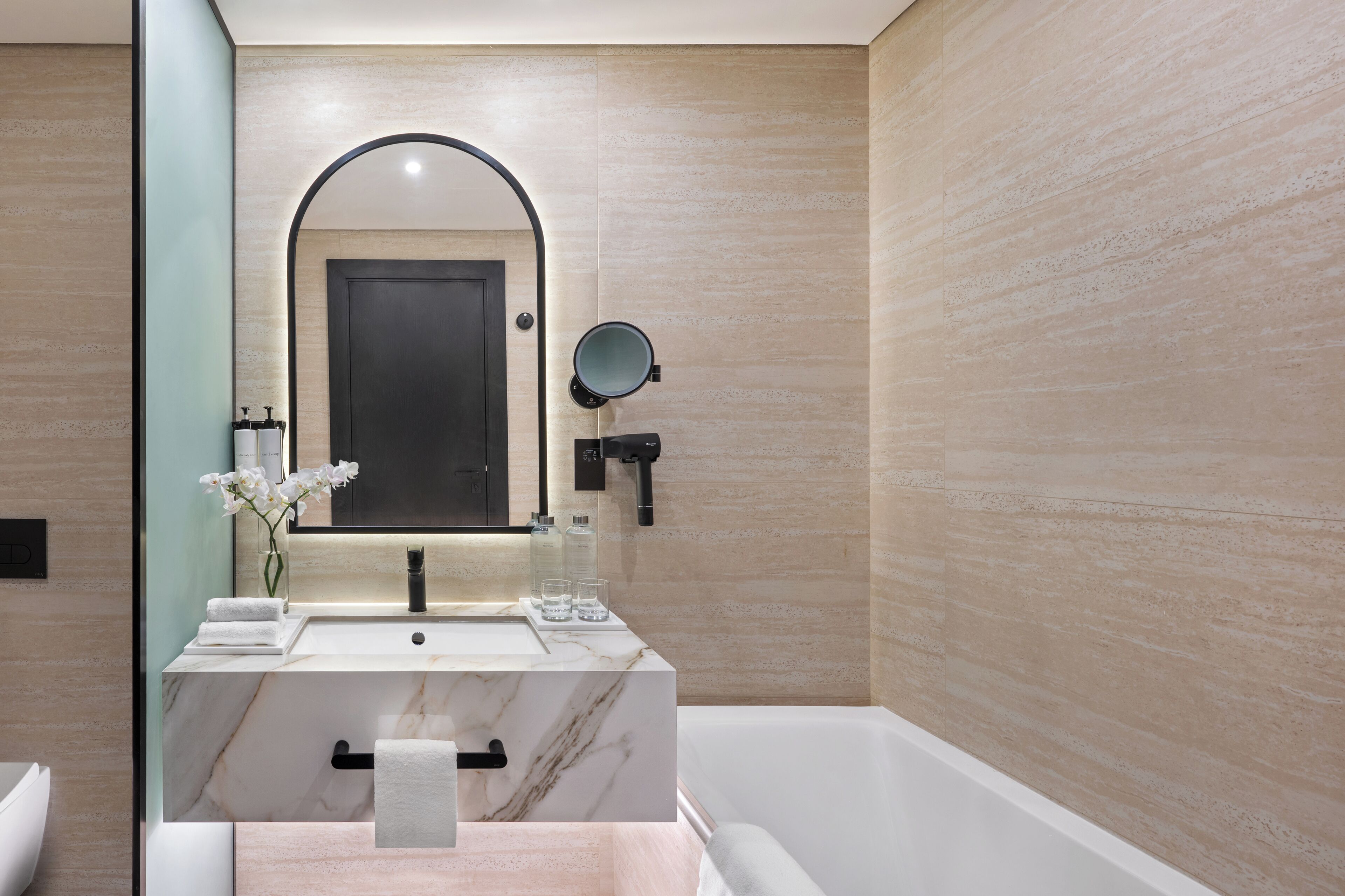 A modern bathroom with a marble sink, a large mirror, and a bathtub.