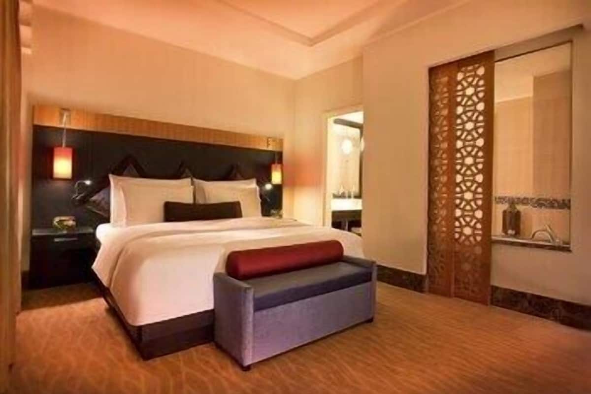 Une chambre d’hôtel avec un grand lit, des tables de chevet, un miroir et un élément de séparation décoratif.