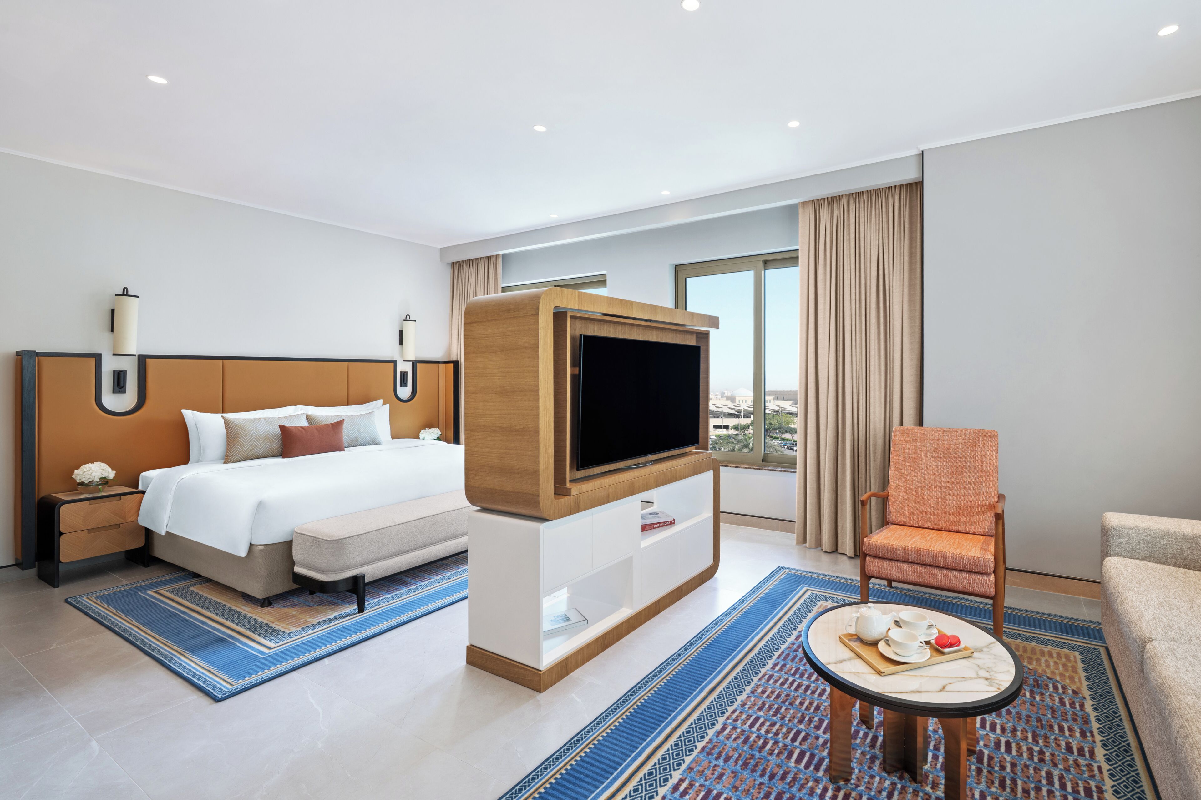 A hotel room with a bed, a TV, a seating area, and a view of the city.