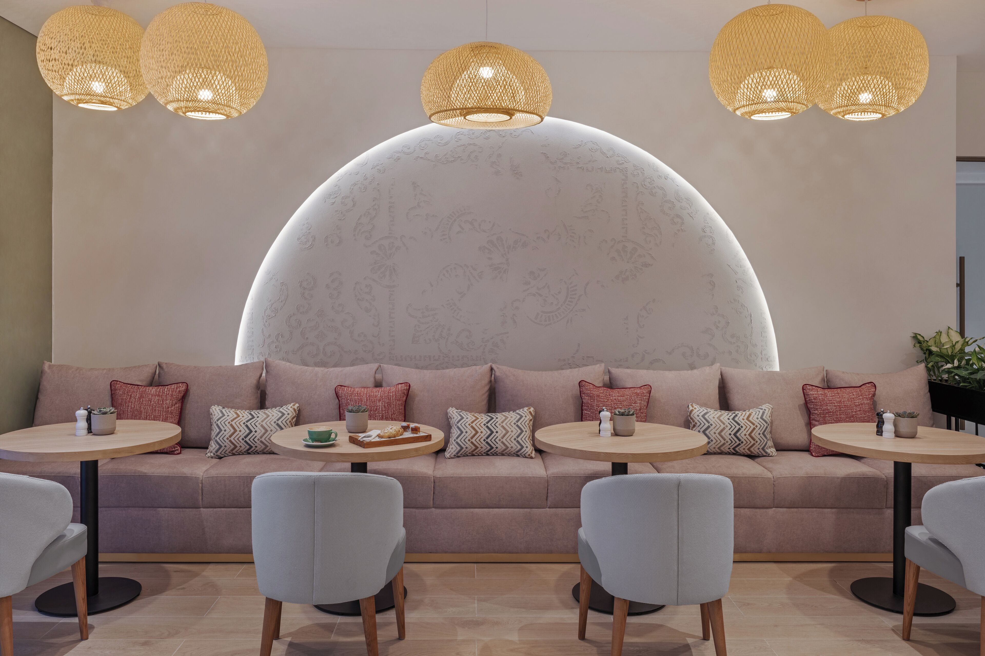 A modern lounge area with a large, semi-circular white wall, two round tables with chairs, and three hanging lamps.