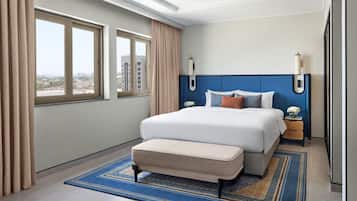 Une chambre d’hôtel moderne avec un grand lit, deux tables de chevet, un banc et une vue sur la ville.
