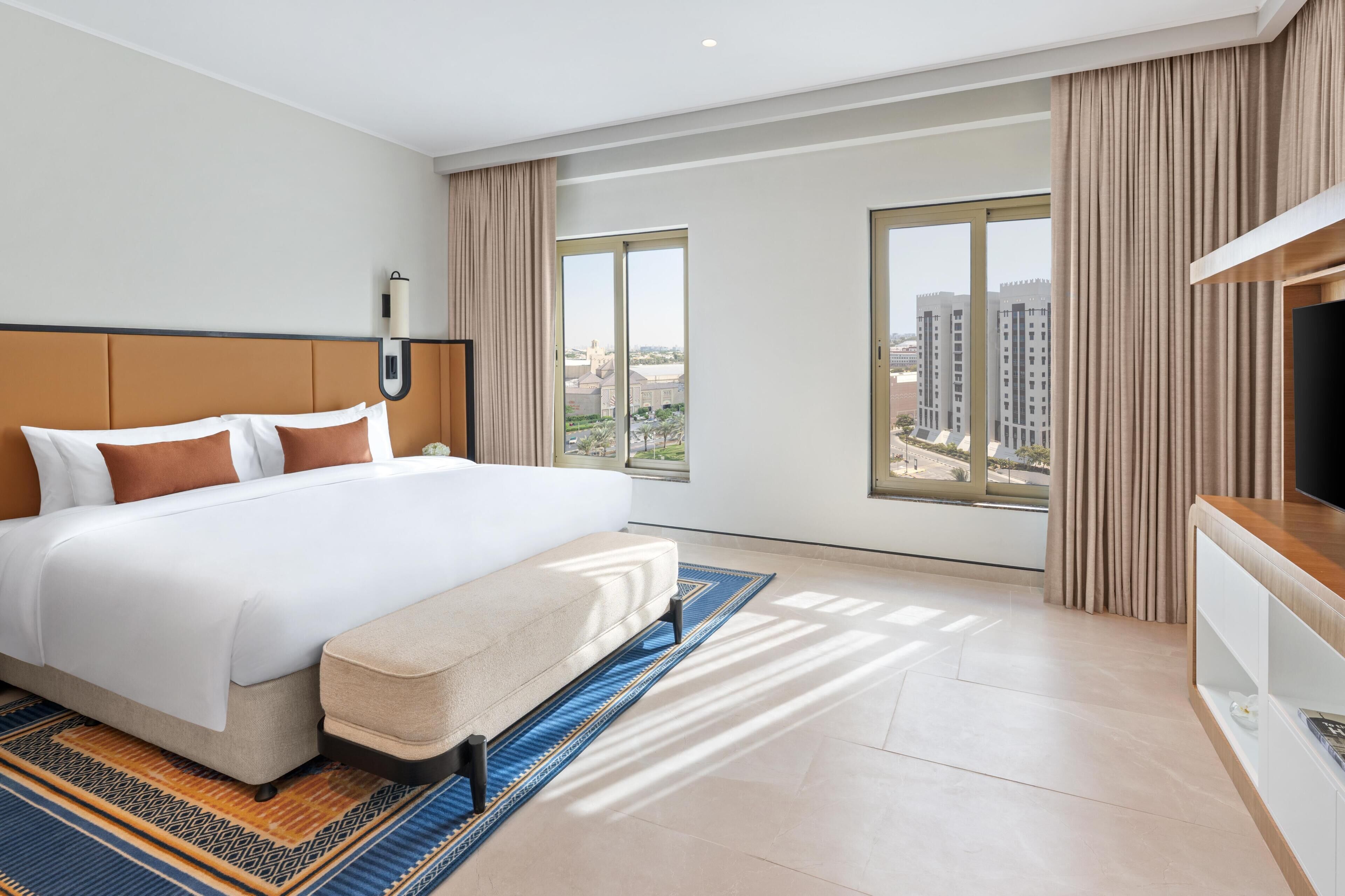 Une chambre d’hôtel moderne dotée d’un grand lit, d’une télévision, d’un bureau et offrant une vue sur la ville.