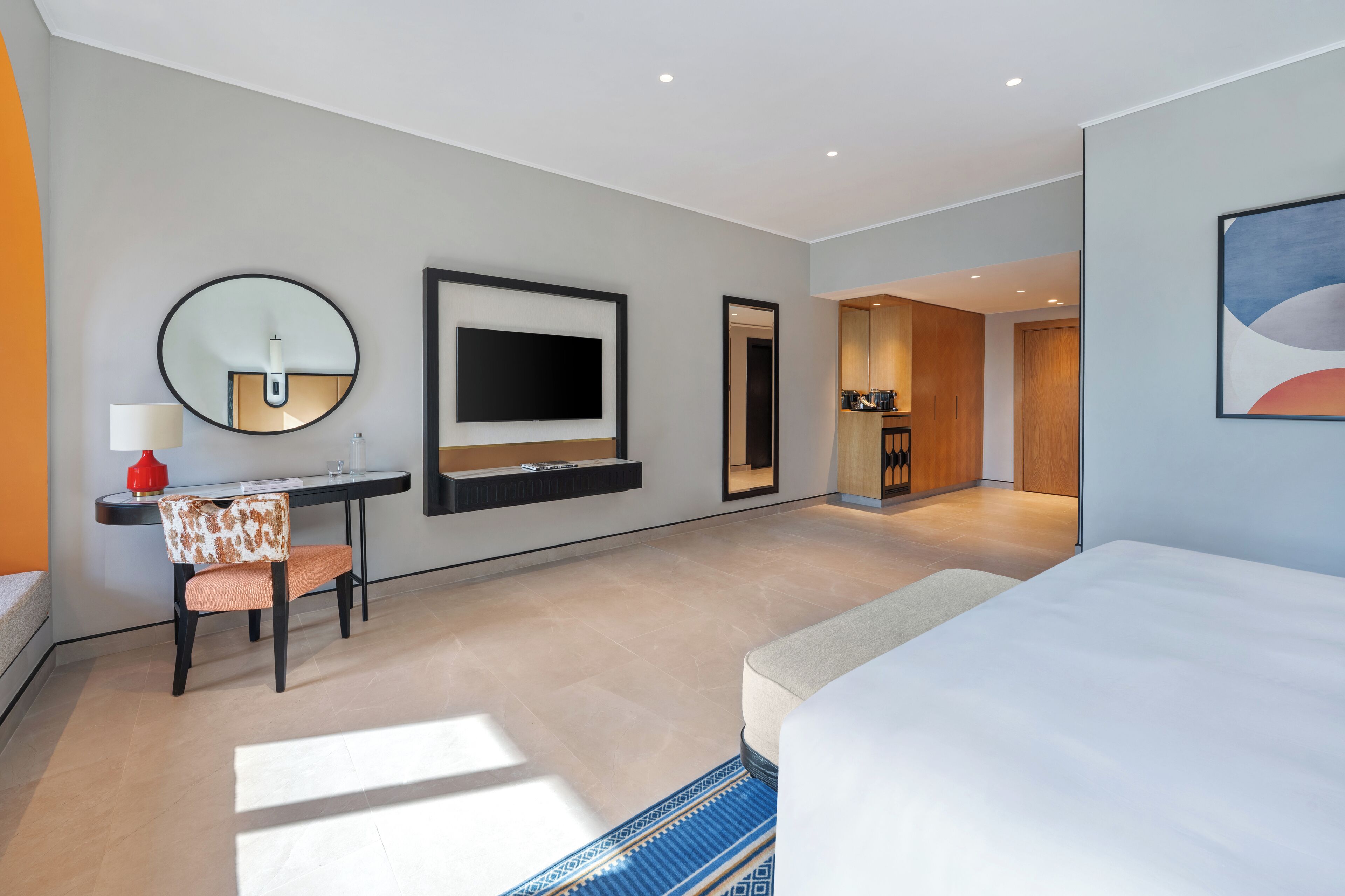 A modern hotel room with a large bed, a desk with a chair, a flat-screen TV, and a large mirror.
