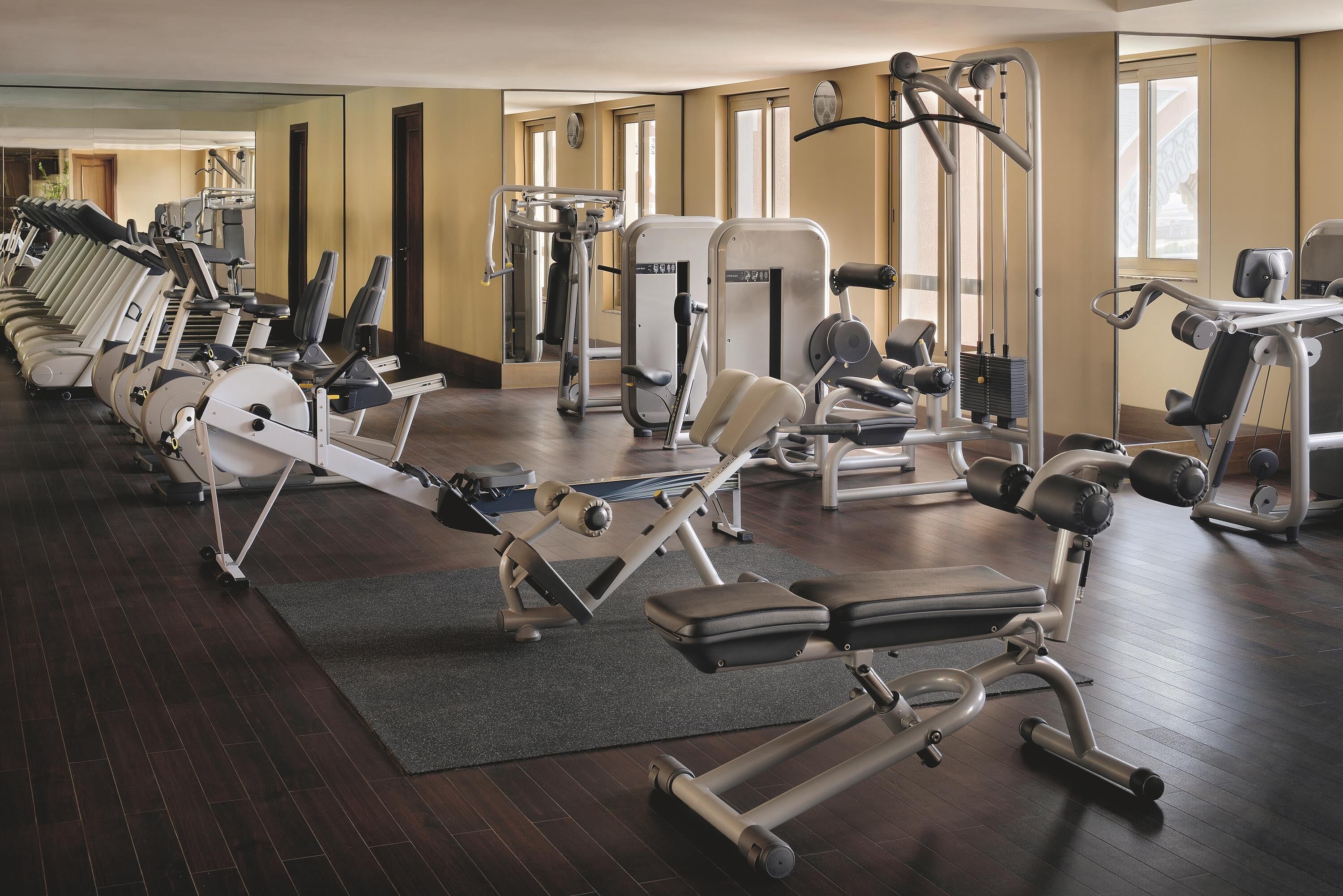 A gym with various exercise machines, a mirror, and a wooden floor.