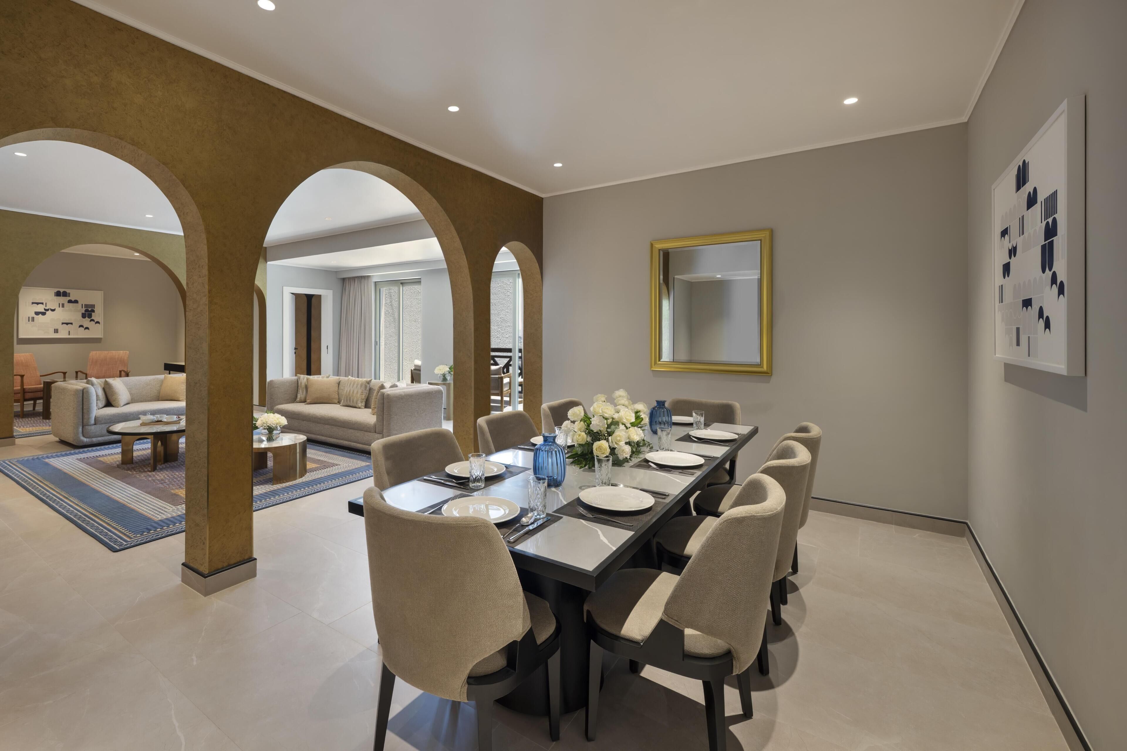 A dining area with a long table, chairs, and a mirror on the wall.