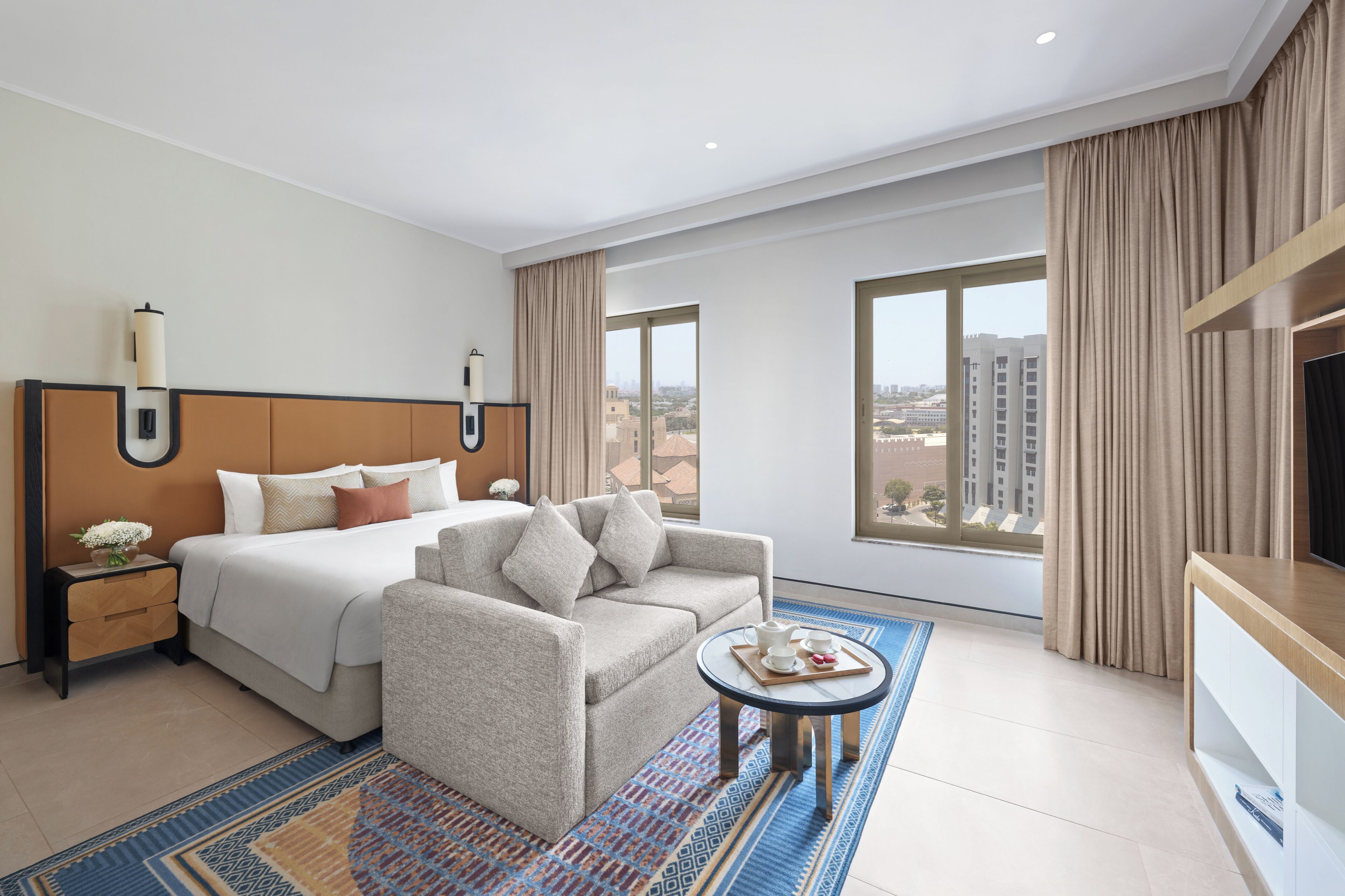 Une chambre d’hôtel avec un lit, un canapé, une petite table avec un plateau, et une télévision.
