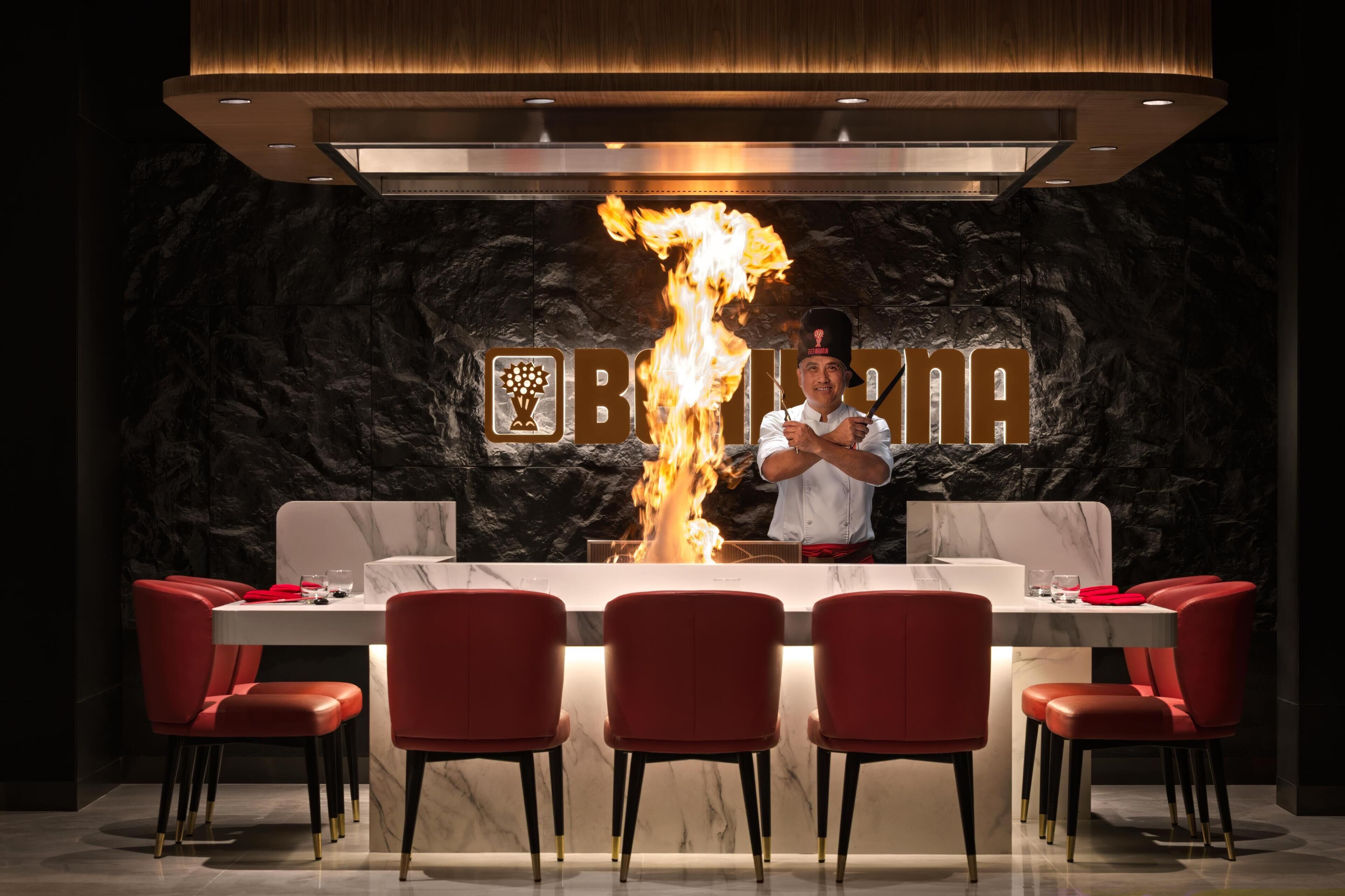 A restaurant with a marble countertop, red chairs, and a chef performing a fire act.