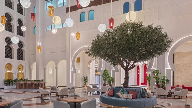 A spacious lobby with a central seating area, multiple tables, and hanging spherical light fixtures.