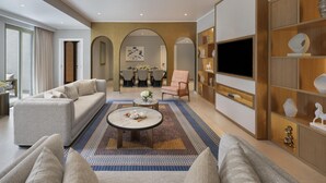 A modern living room with a sofa, armchairs, a coffee table, and a TV. There is a dining area in the background with a table and chairs.