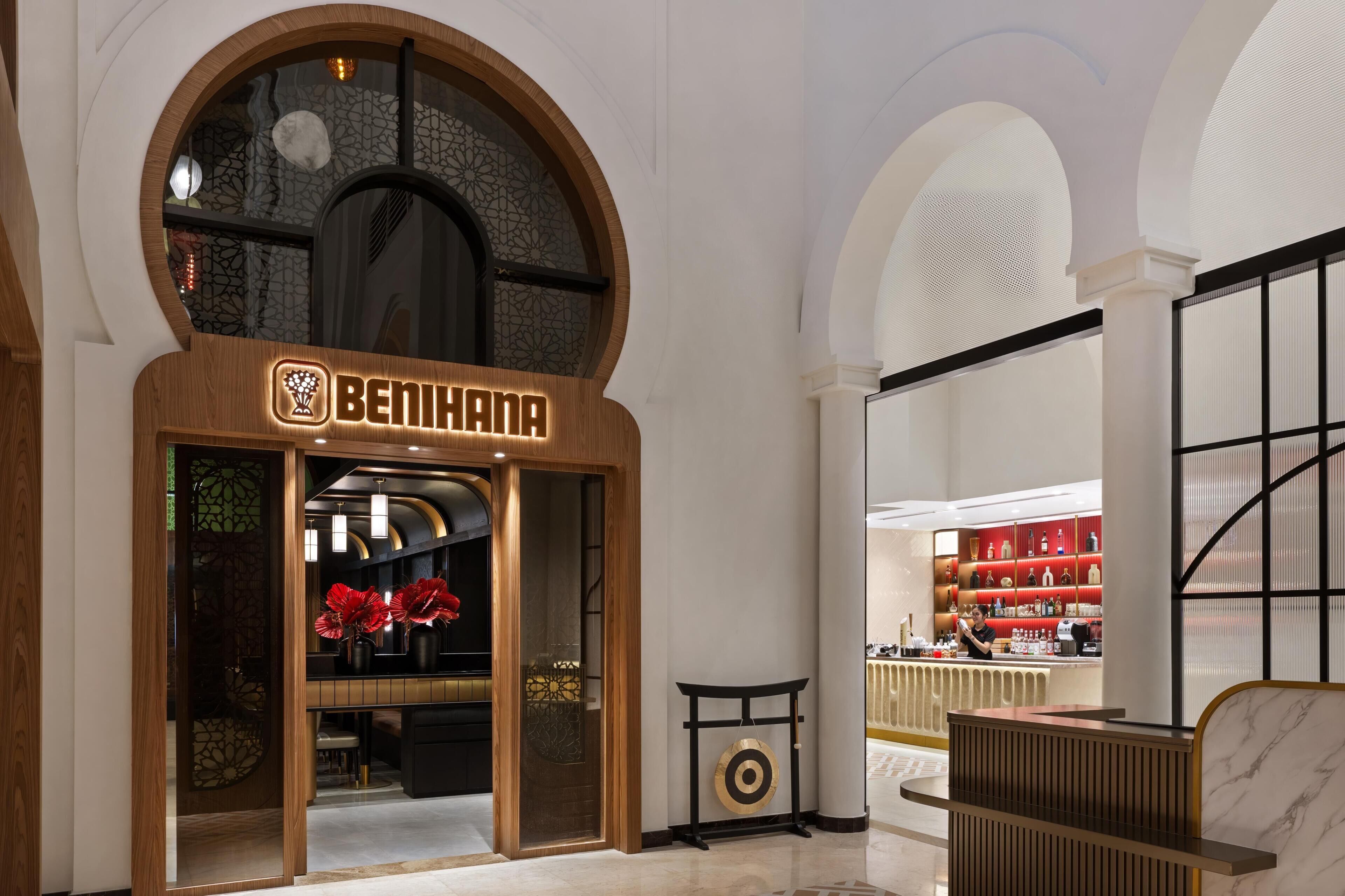 A hotel interior with a reception desk, a store with red items, and a decorative wall with a circular pattern.