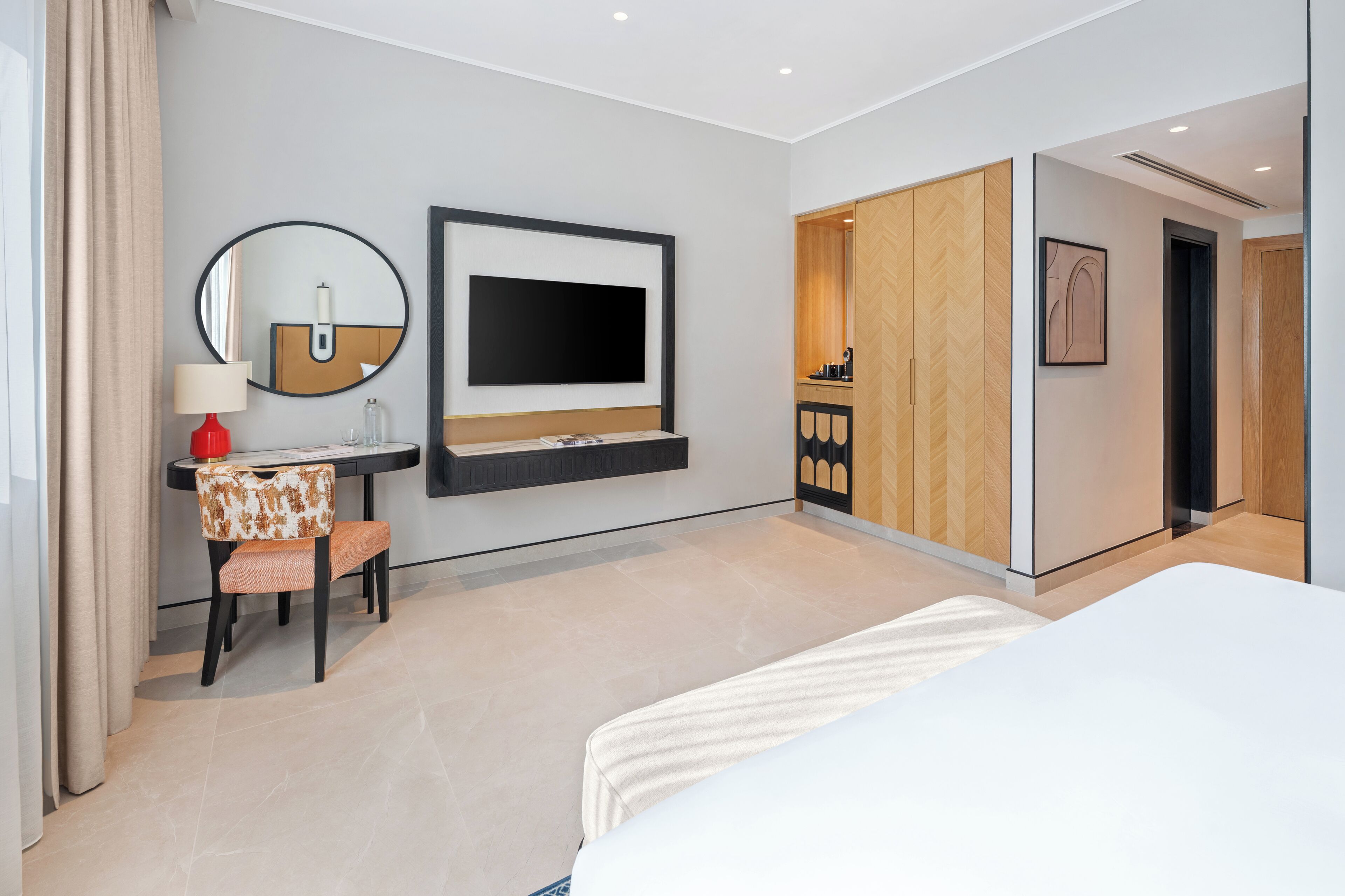 Een moderne hotelkamer met een bed, een bureau met stoel, een televisie en een spiegel.