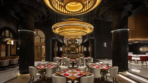 A spacious restaurant with high ceilings, a central chandelier, and a bar area.