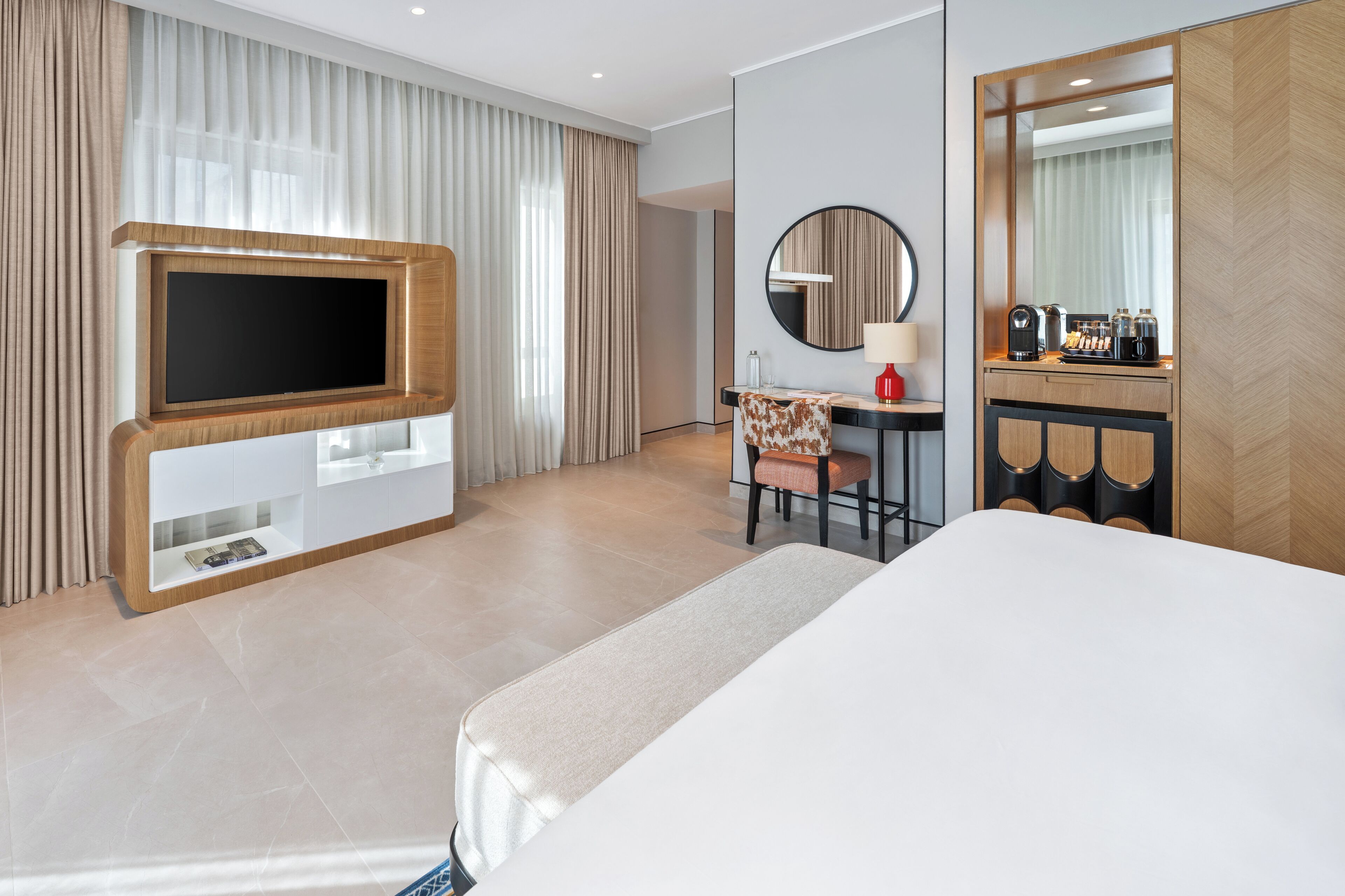 Une chambre d’hôtel équipée d’un grand téléviseur à écran plat, d’un bureau avec une chaise, d’une machine à café et d’un miroir.