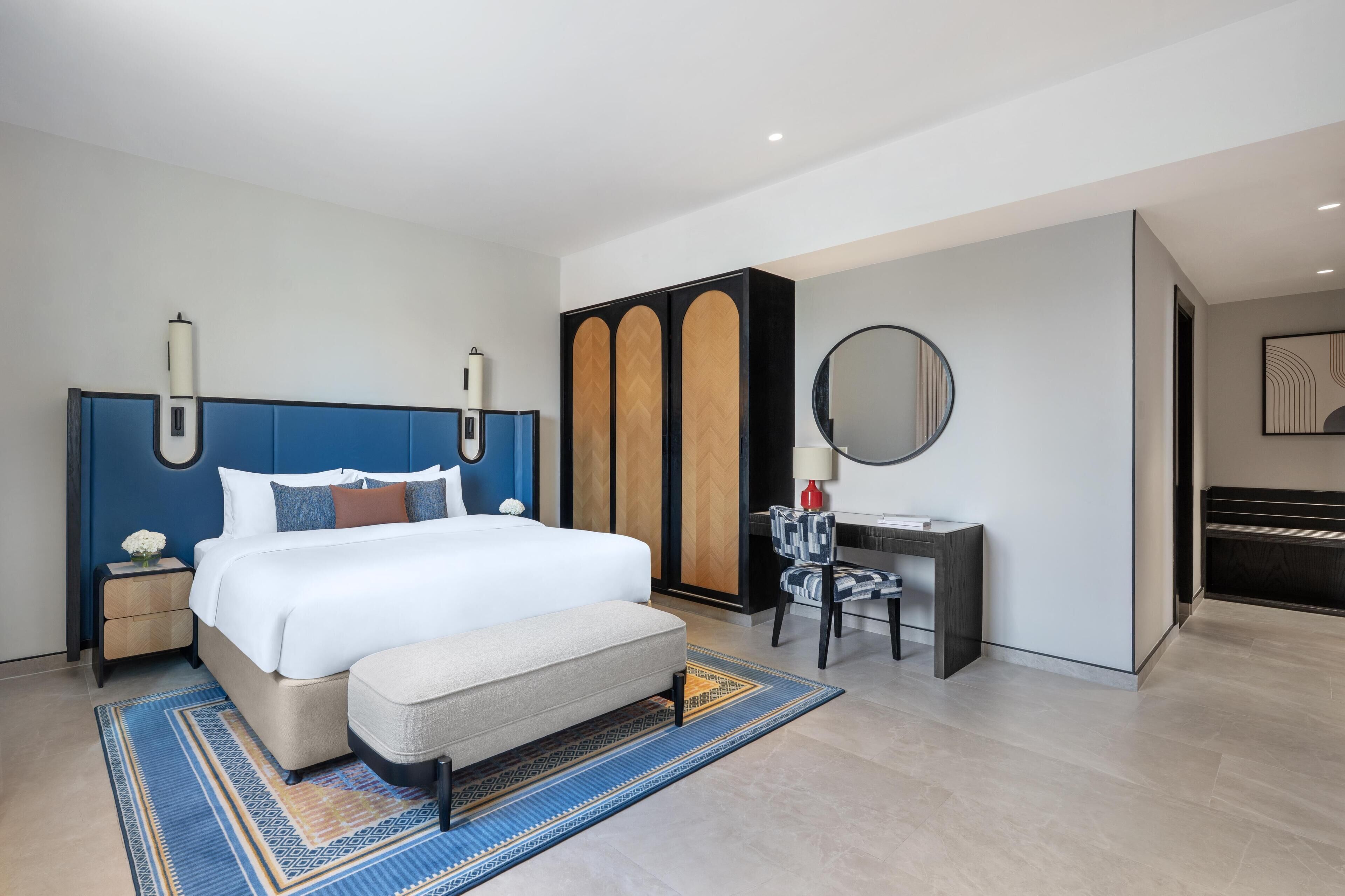 Een moderne hotelkamer met een groot bed, nachtkastje, bureau en spiegel.