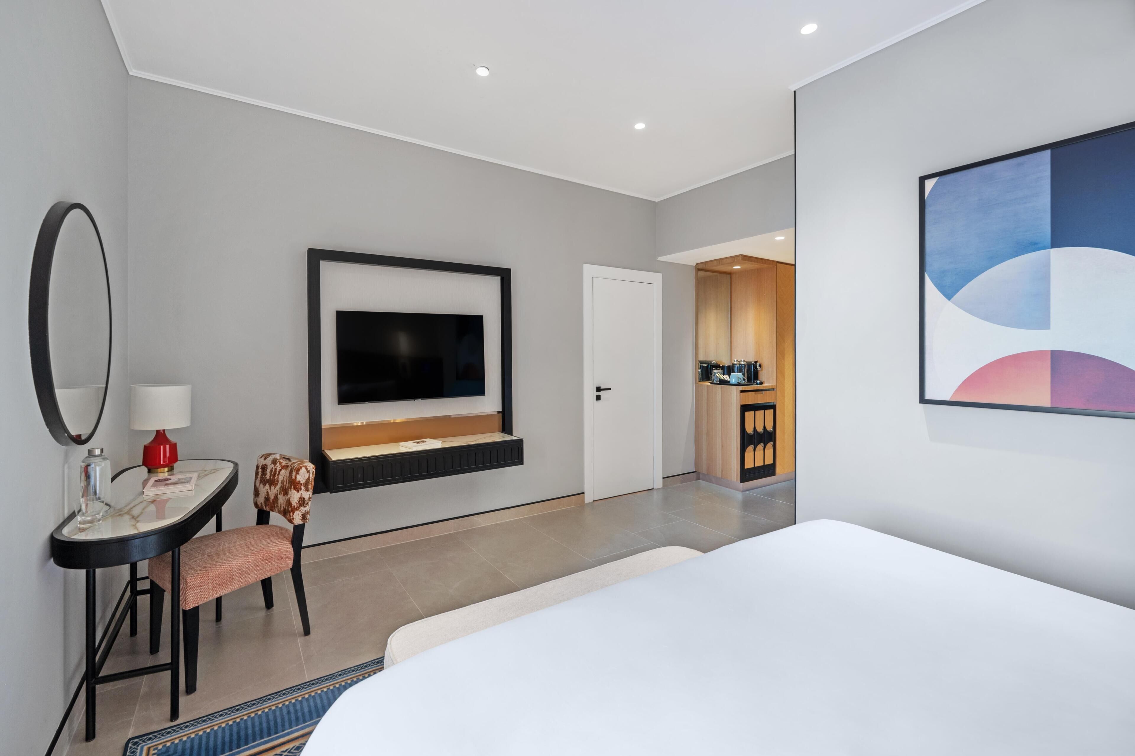 Une chambre d’hôtel moderne équipée d’un lit, d’un téléviseur fixé au mur, d’un bureau avec une chaise et d’une petite table avec une lampe.
