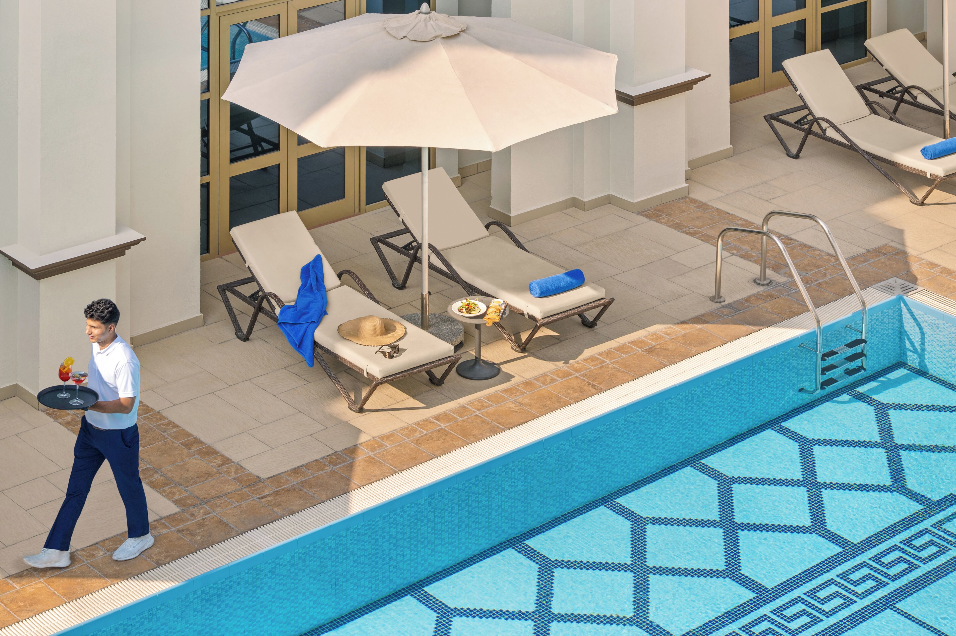 Zona de piscina con sillones de descanso, una bandeja de servicio y una piscina con baldosas.