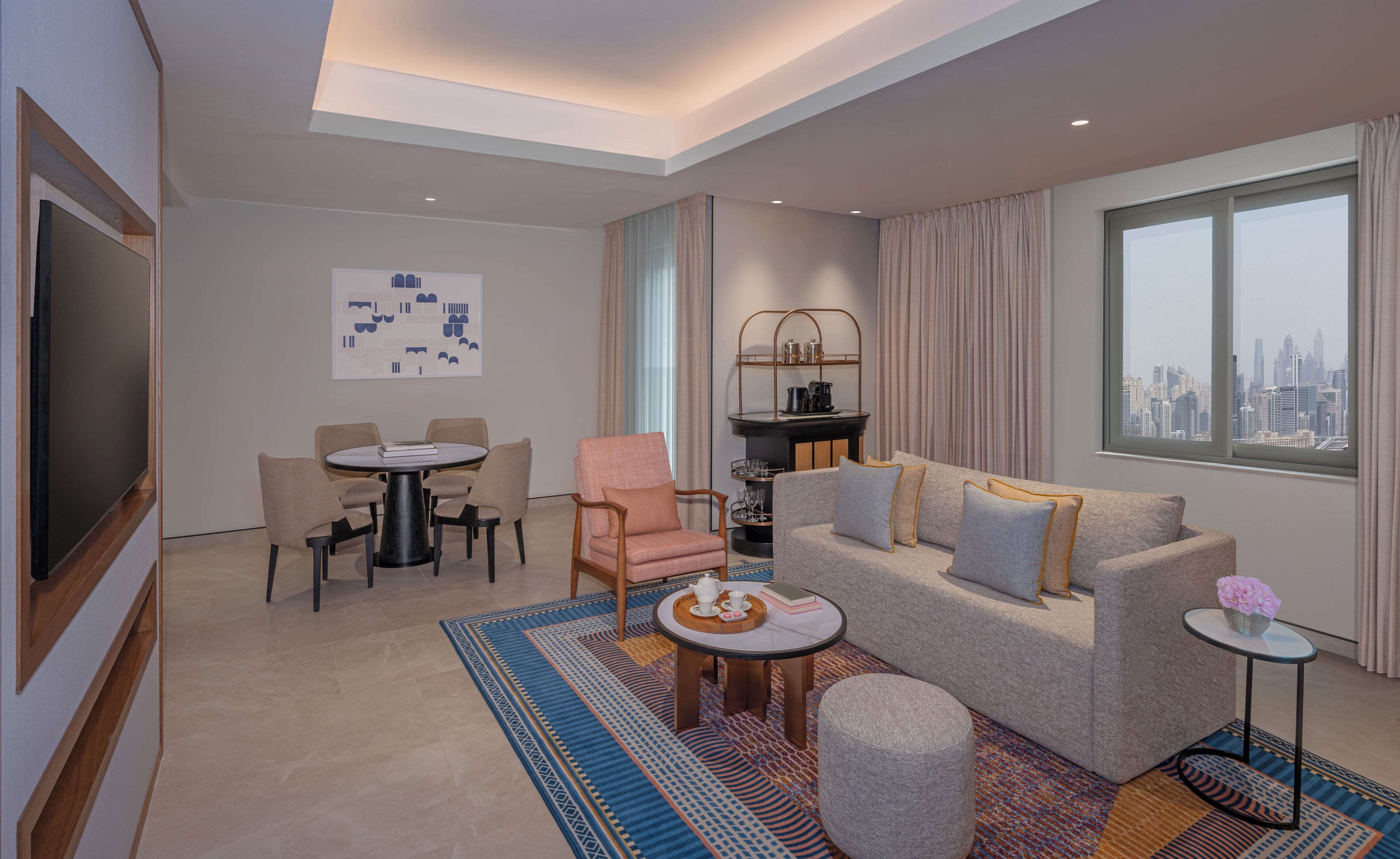 Een moderne hotelkamer met uitzicht over de stad, een eethoek met een ronde tafel, een bank en een klein bijzettafeltje met bloemen.